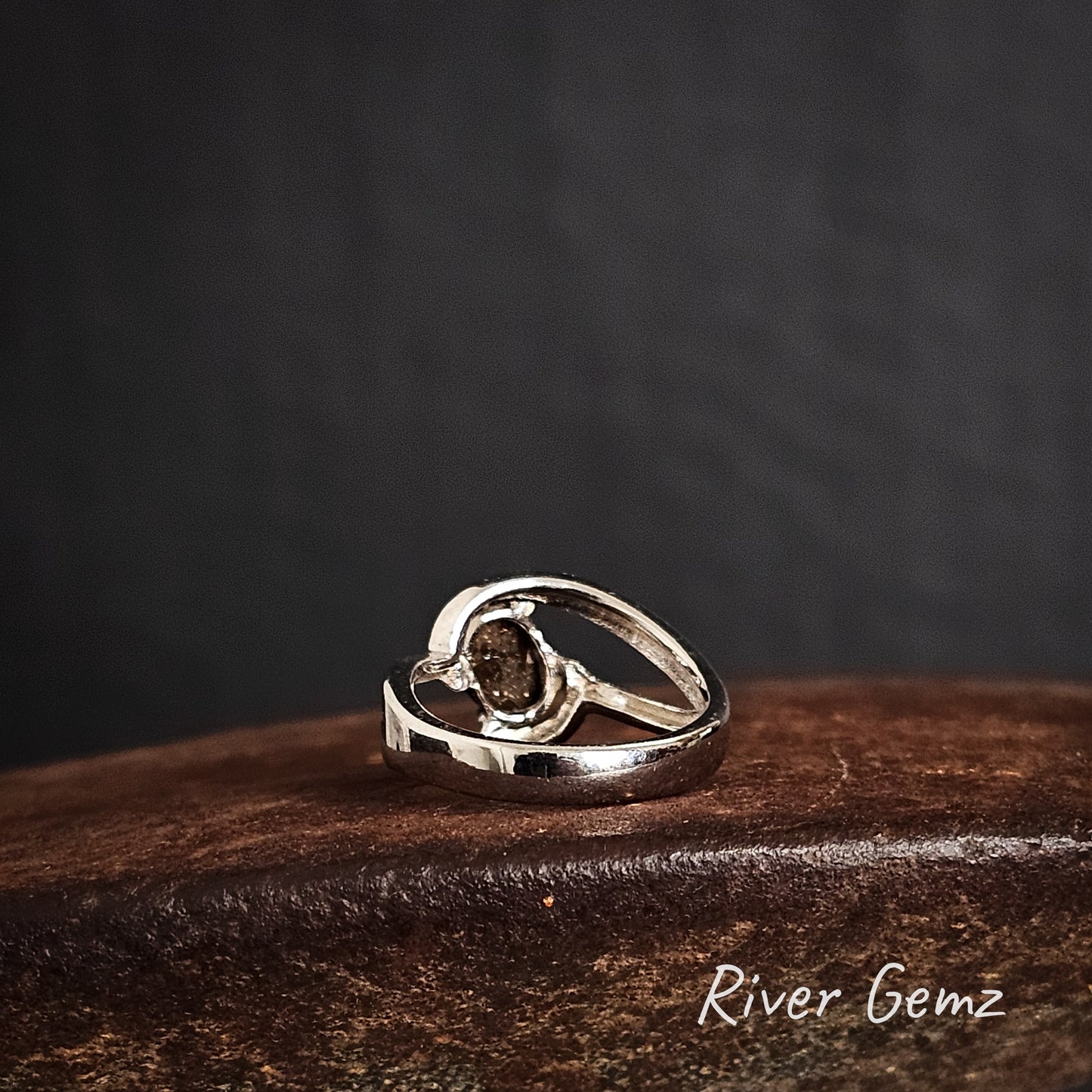 Rear view of silver ring showing the ironstone matrix of the boulder opal on a brow surface with a dark background