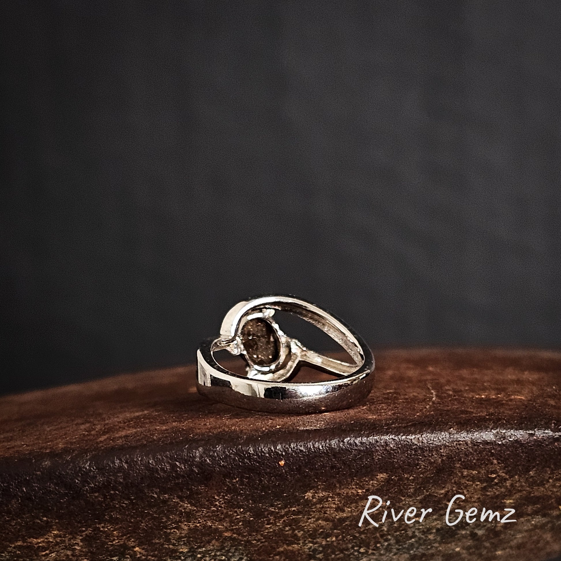 Rear view of silver ring showing the ironstone matrix of the boulder opal on a brow surface with a dark background