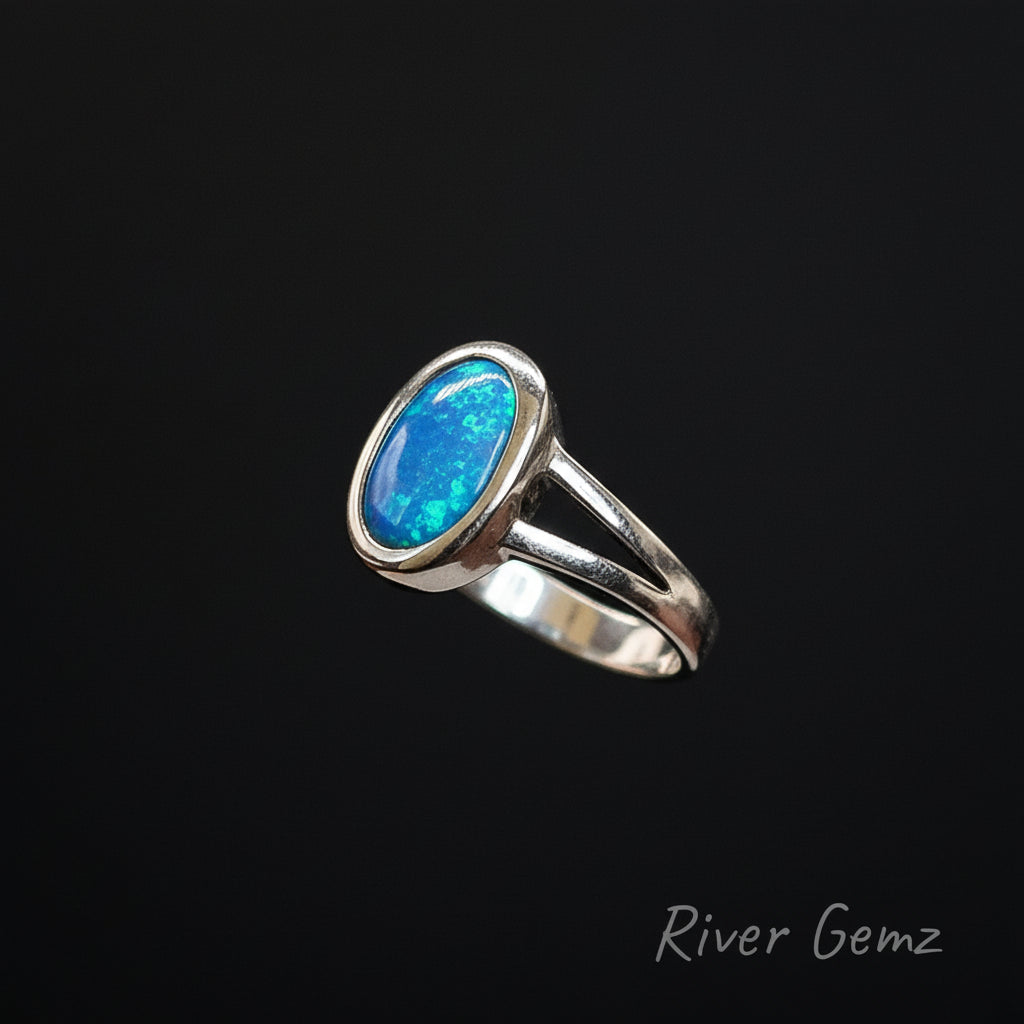Silver ring with a blue stone on a black stand, branded 'River Gemz'.