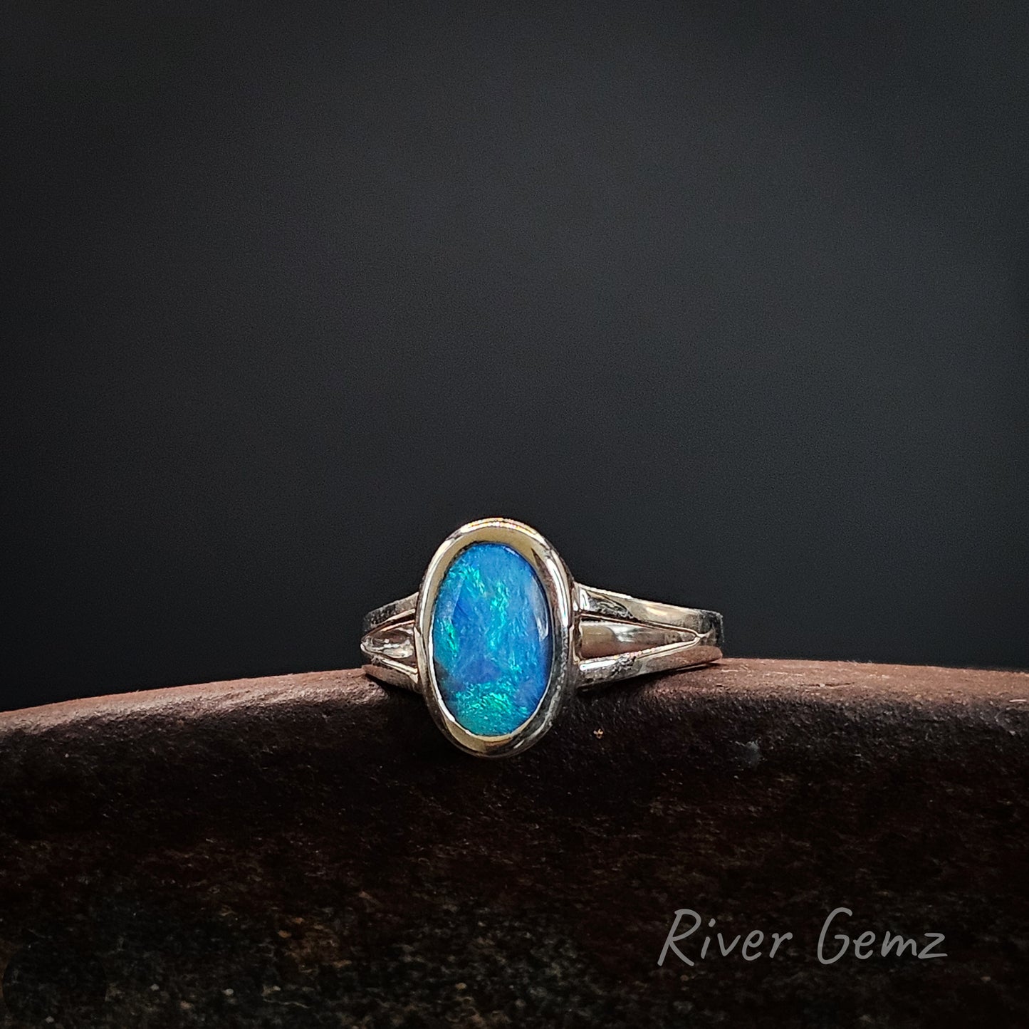 Silver ring with a blue opal stone on a dark background, branded 'River Gemz'.
