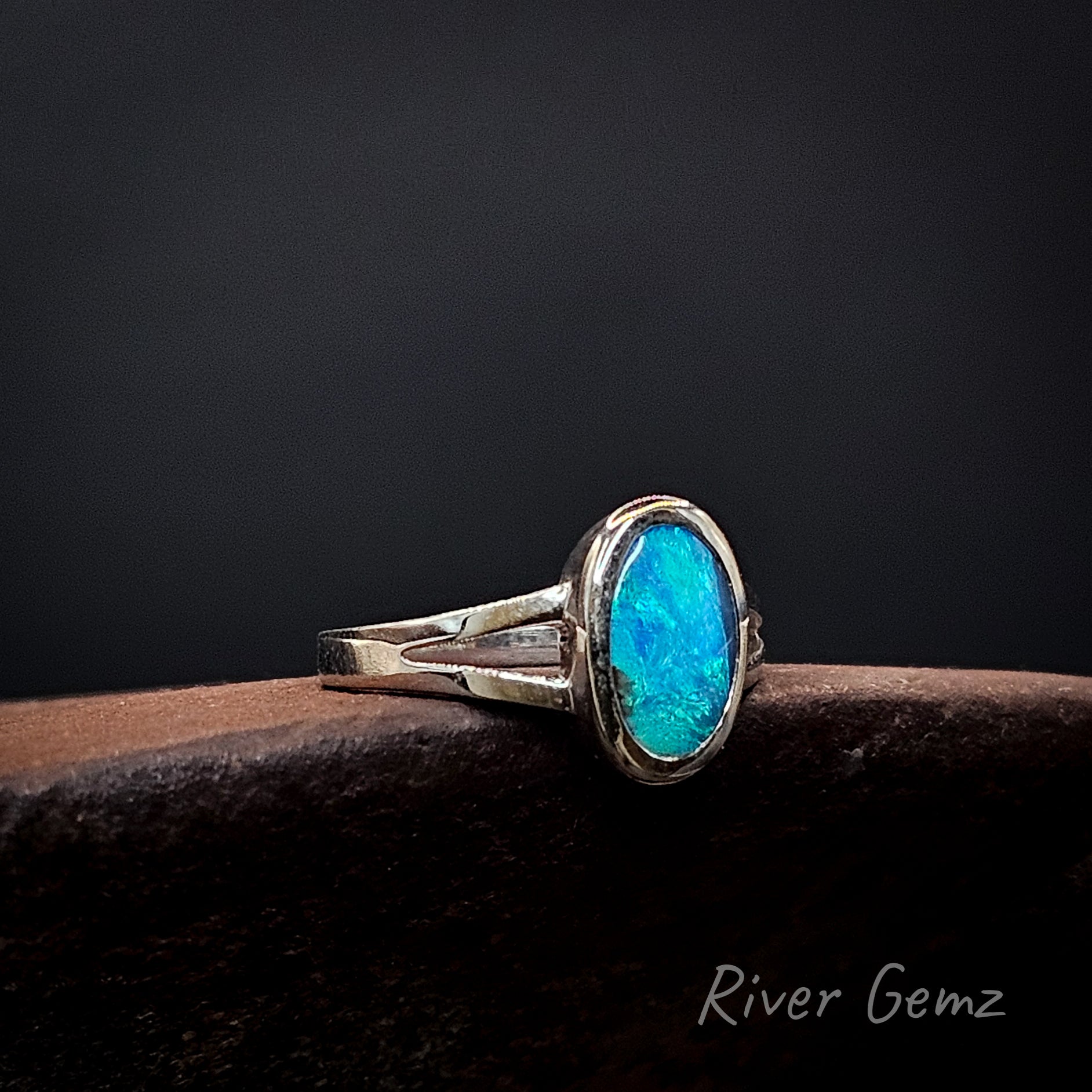 Silver ring with a blue stone on a dark background, featuring 'River Gemz' branding.
