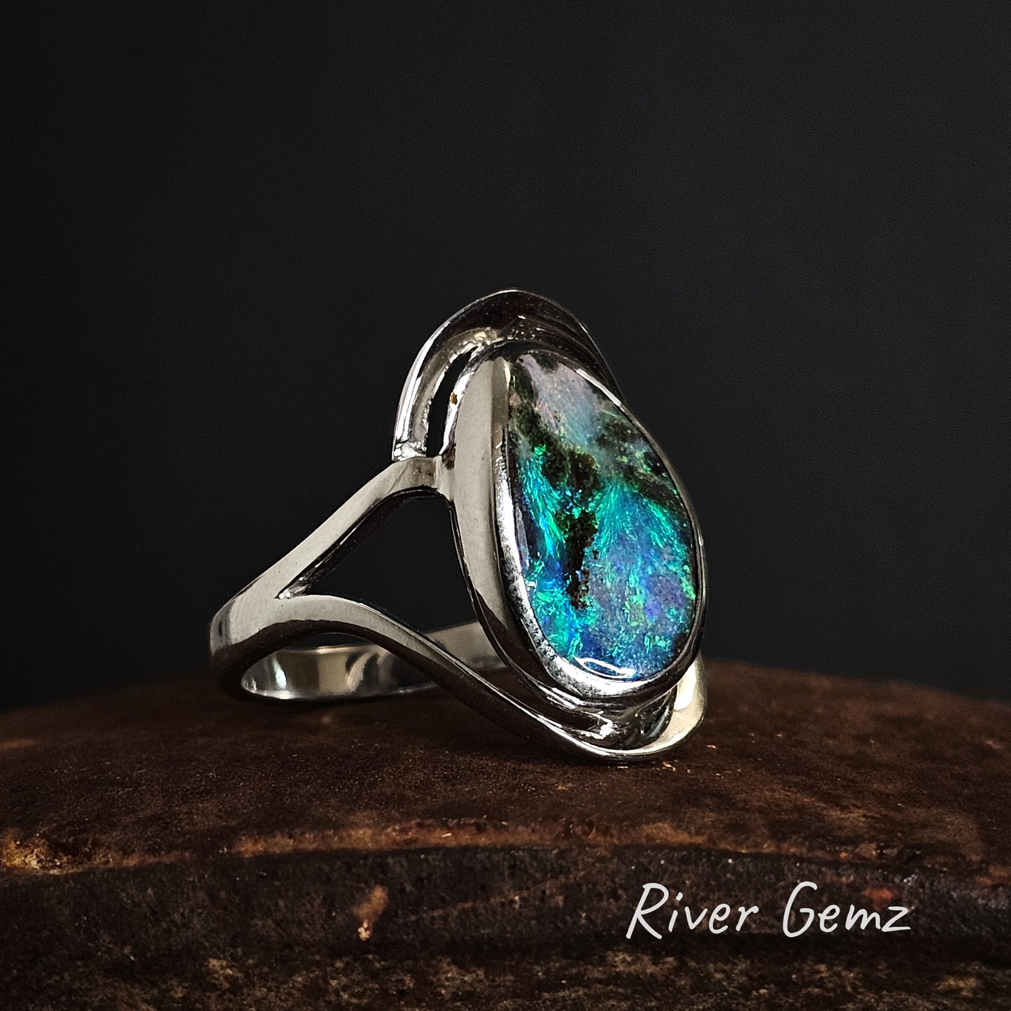 Sterling silver ring with a colourful boulder opal on a dark background, branded 'River Gemz'.