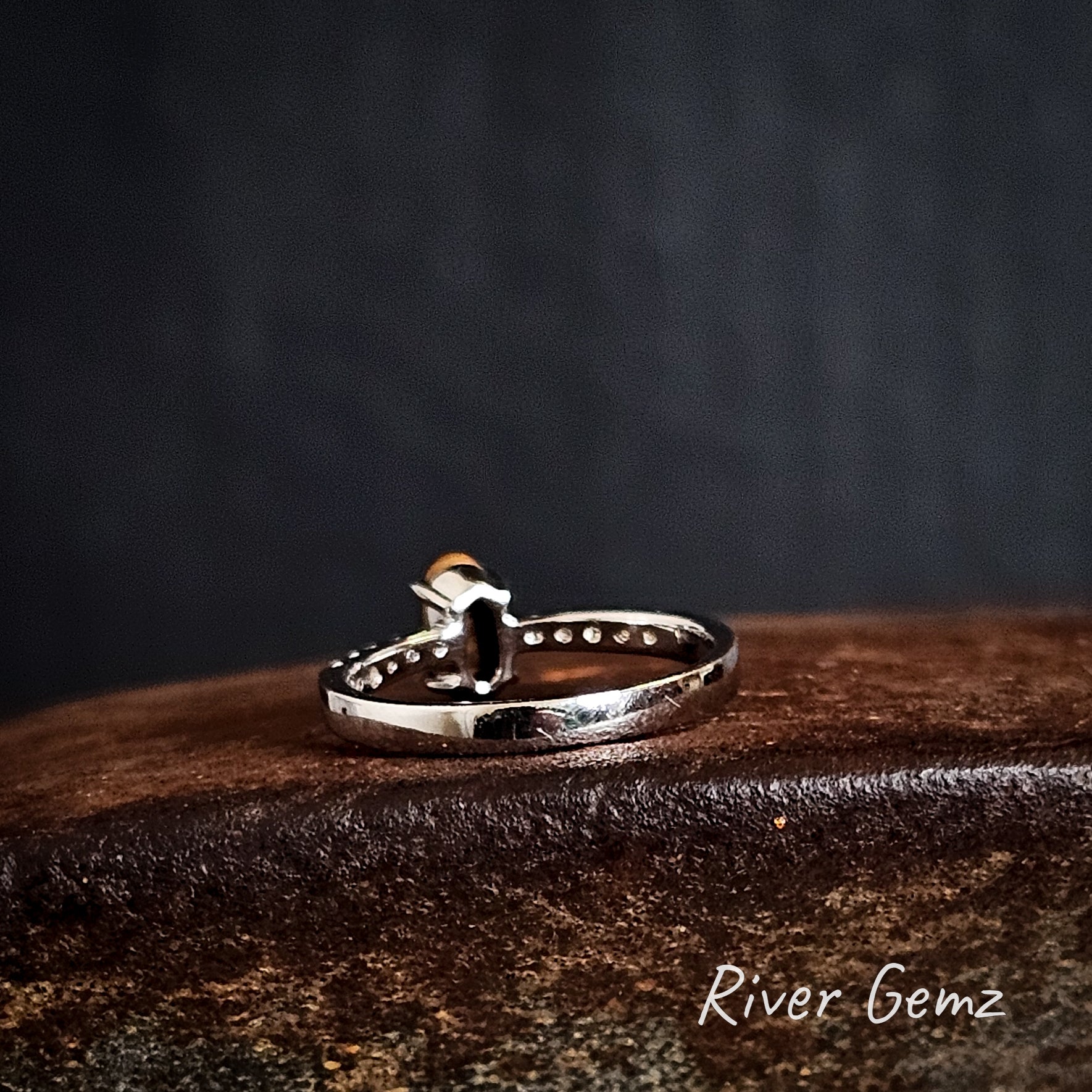 Back of silver ring showing the ironstone matrix of the boulder opal on a dark surface, branded 'River Gemz'.