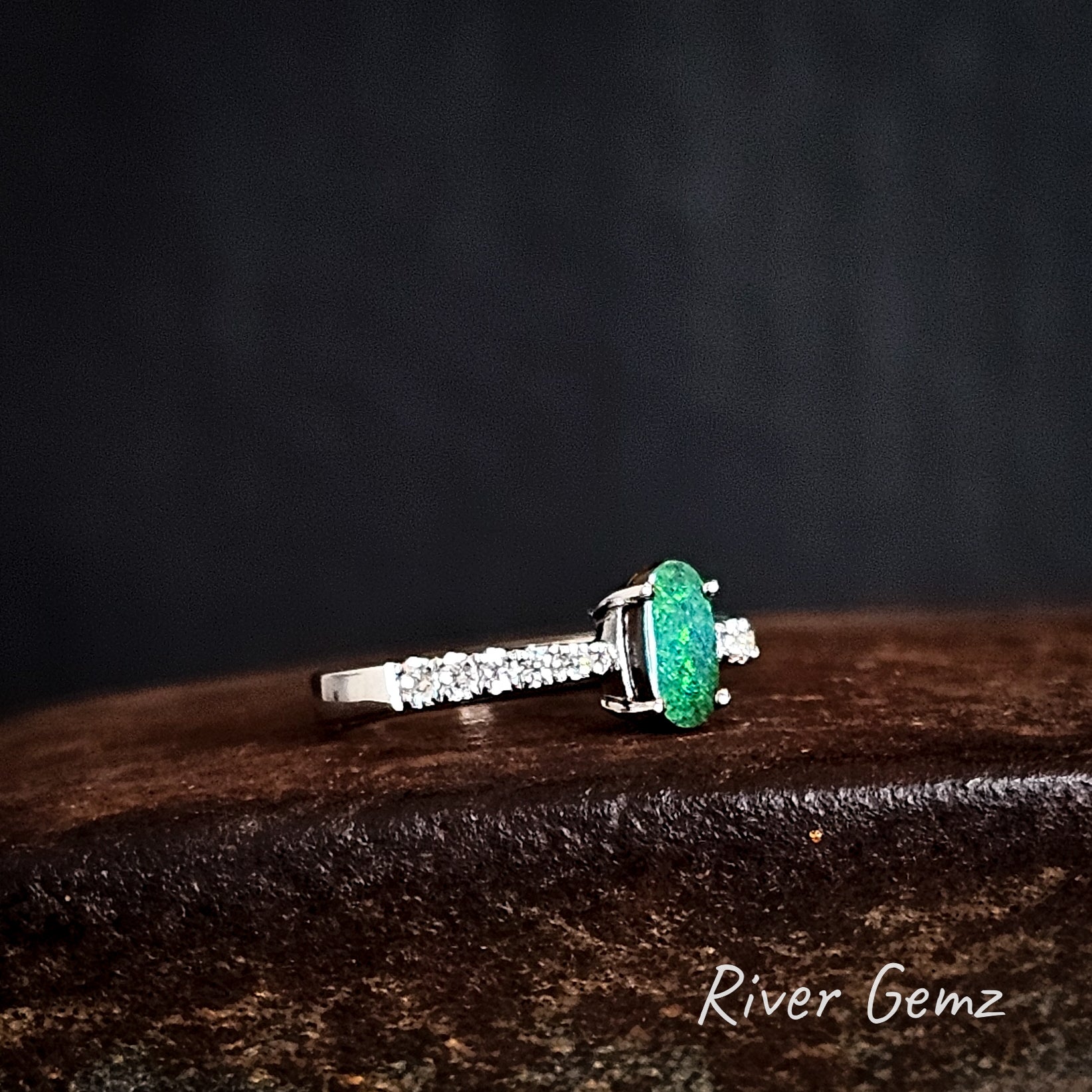Ring with an oval shaped green gemstone on a dark background, featuring the brand 'River Gemz'.