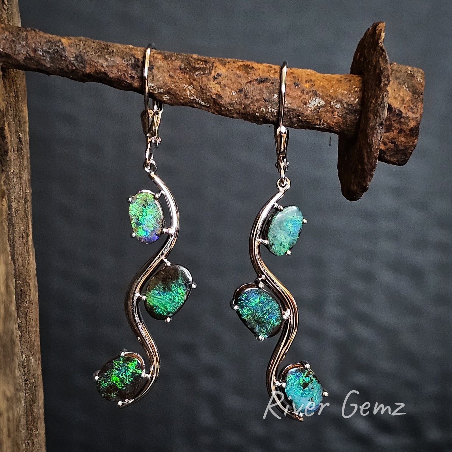 Three oval shaped green opals claw set in a winding river setting of these silver dangly earrings.