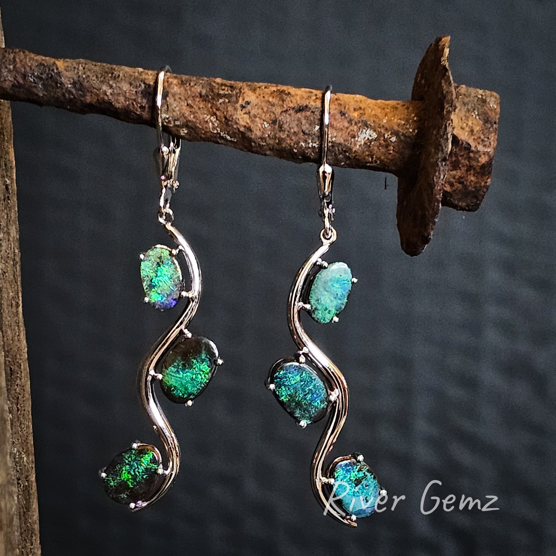 A pair of long dangly silver earrings with 3 oval shaped green opals claw set in each hook earring.