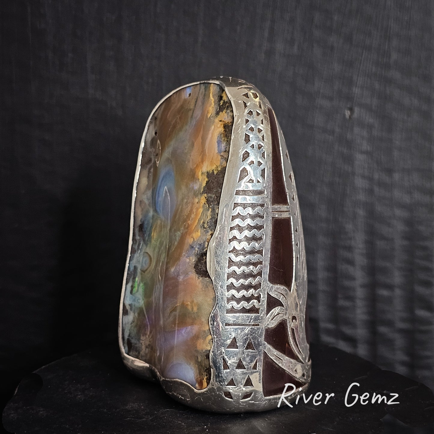 Decorative stone with silver inlay on a dark background, featuring 'River Gemz' branding.