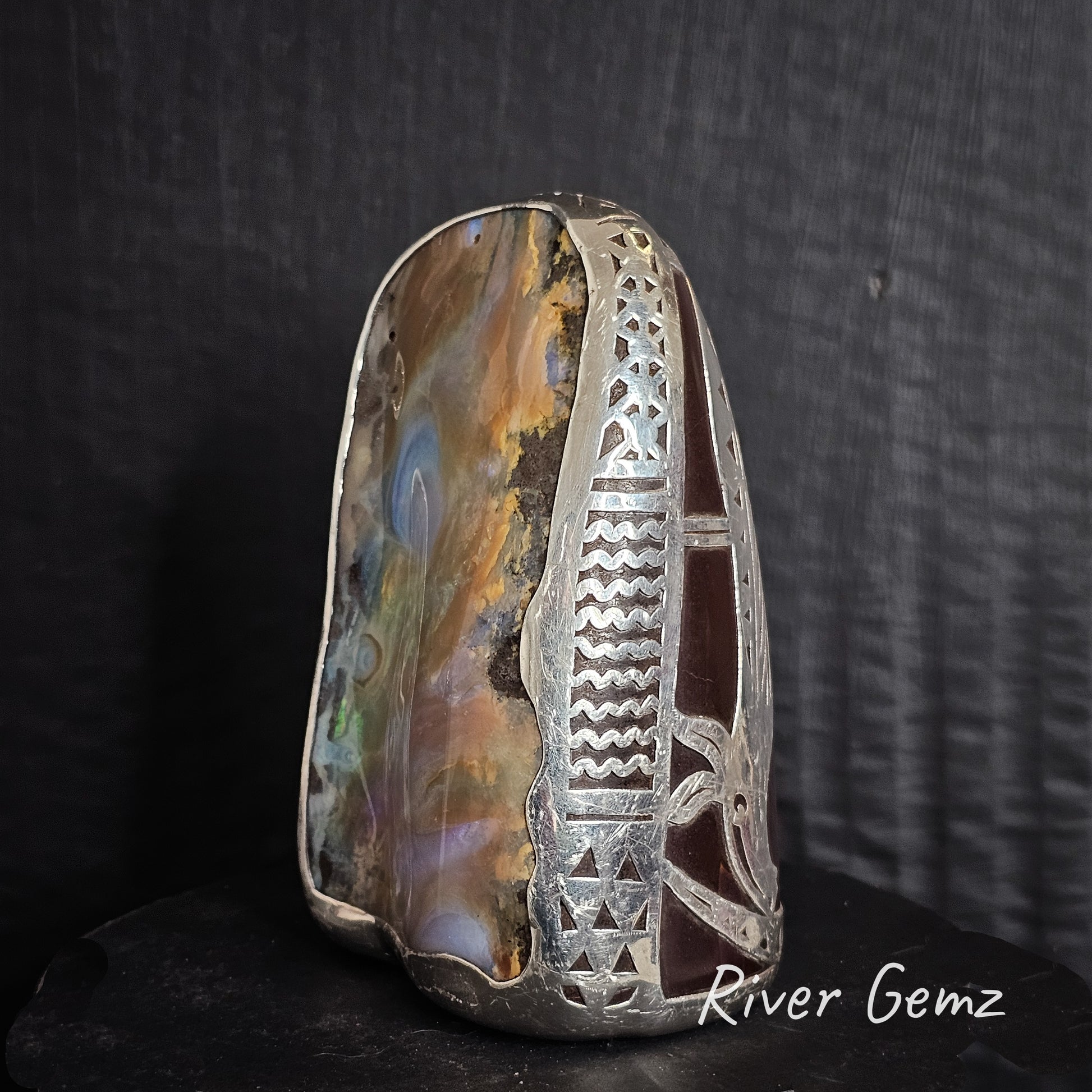 Decorative stone with silver inlay on a dark background, featuring 'River Gemz' branding.