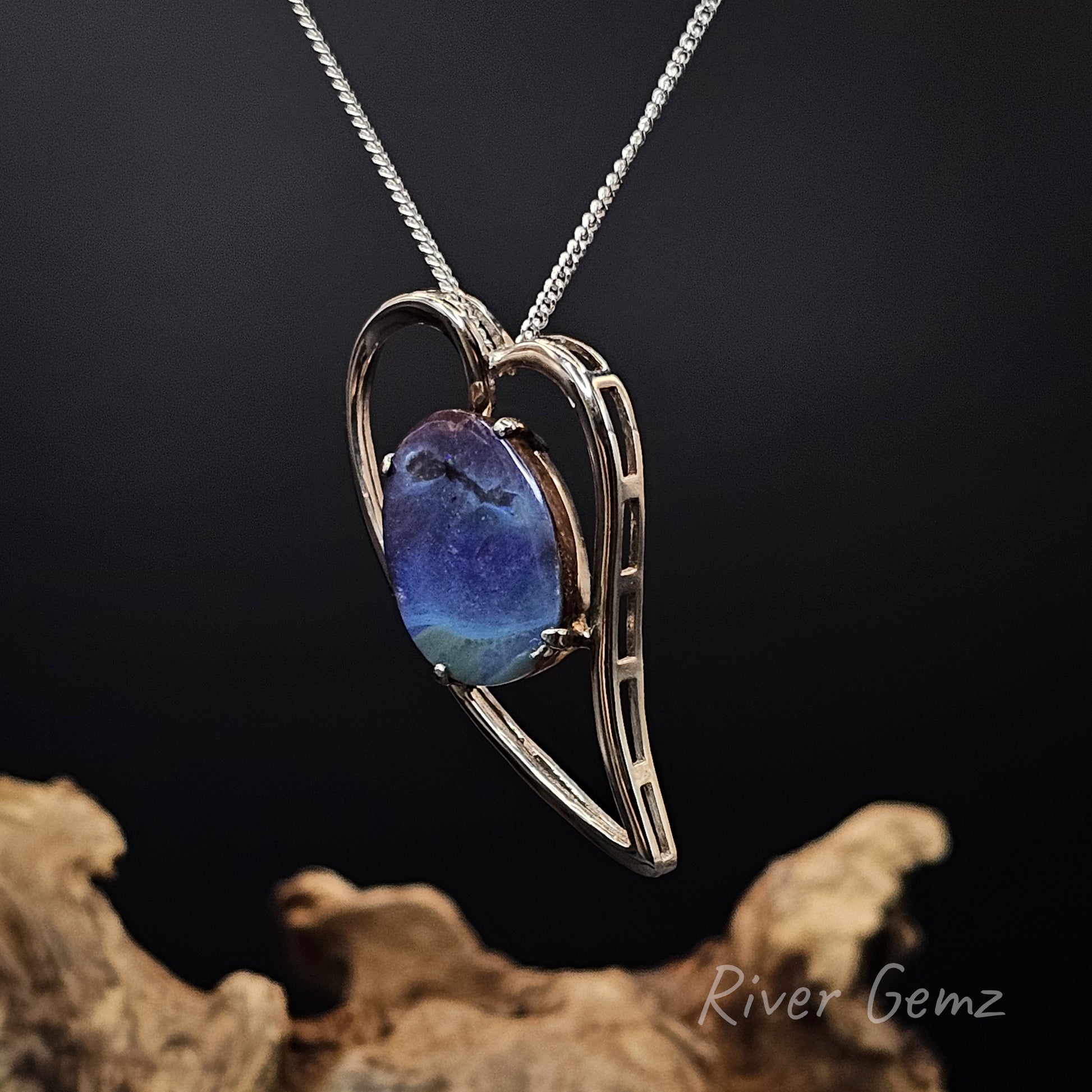 Silver necklace with a heart-shaped pendant featuring a blue stone, set against a dark background.