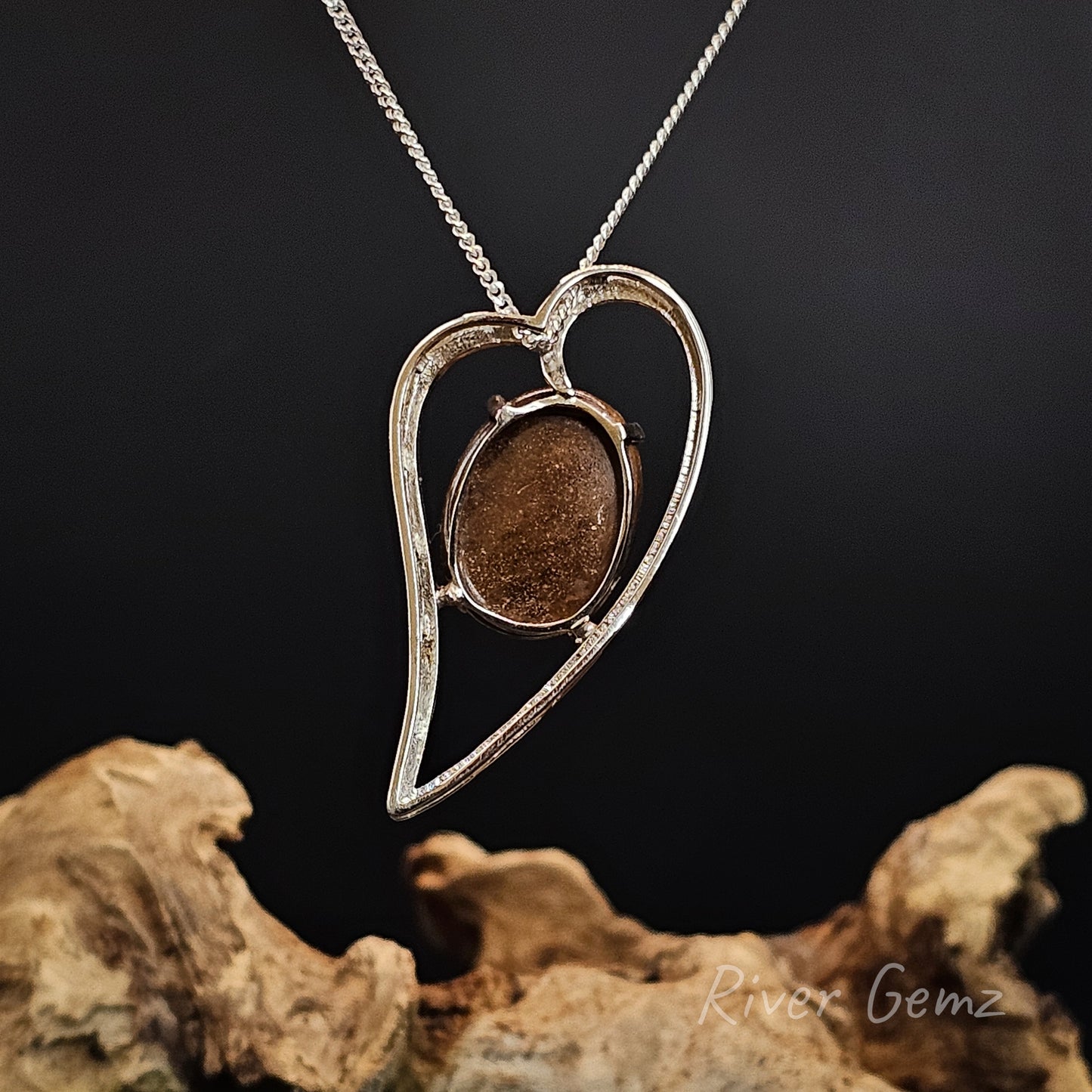 Silver heart-shaped pendant with a brown stone on a dark background