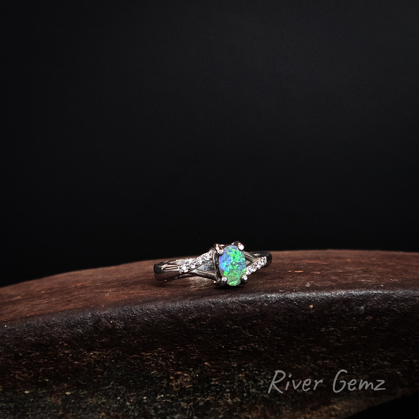 Green and blue oval shaped boulder opal claw set in silver ring with white topaz shoulders.