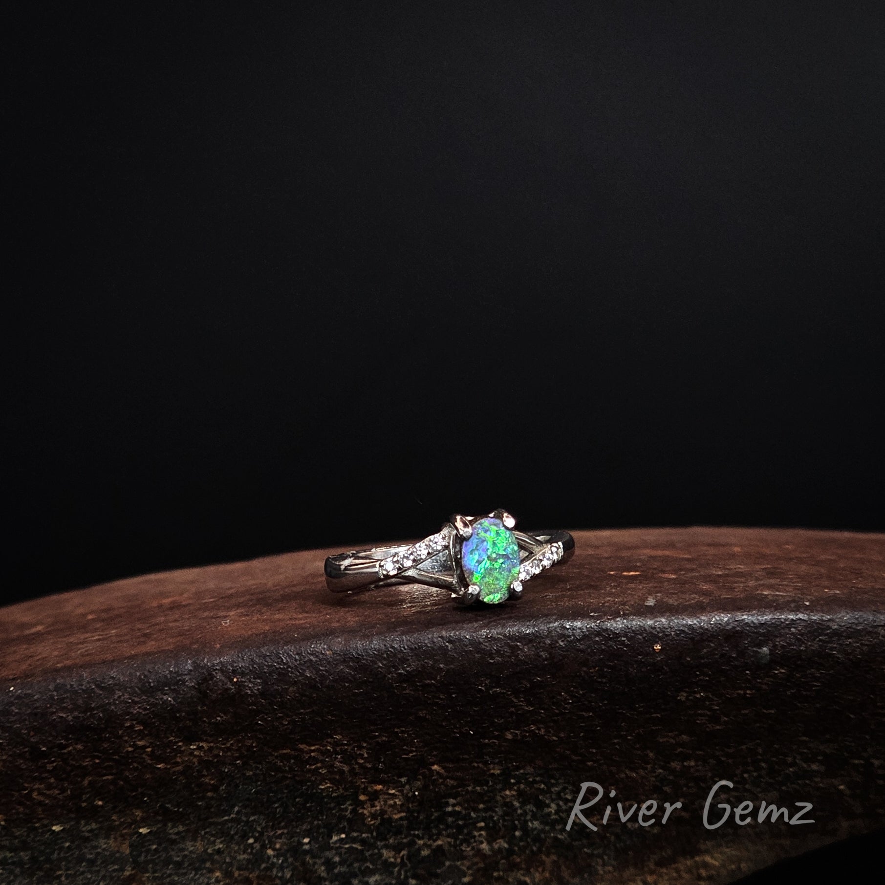 Green and blue oval shaped boulder opal claw set in silver ring with white topaz shoulders.