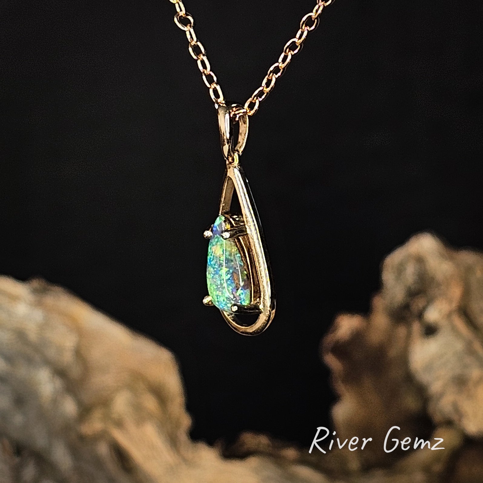 Gold pendant with a green gemstone on a dark background, featuring 'River Gemz' branding.