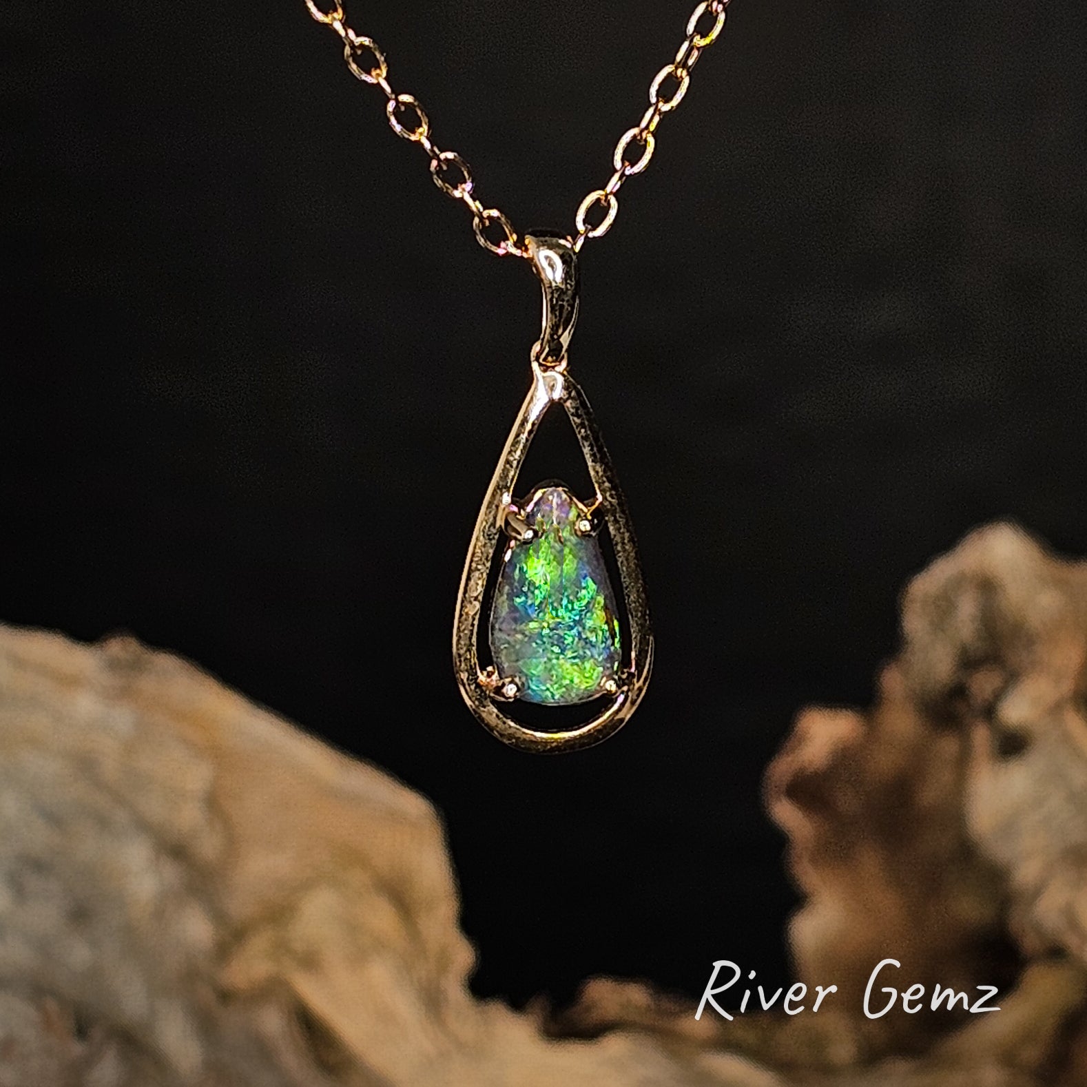 Teardrop-shaped gold pendant with a claw set green boulder opal on a chain, set against a dark background with 'River Gemz' branding.