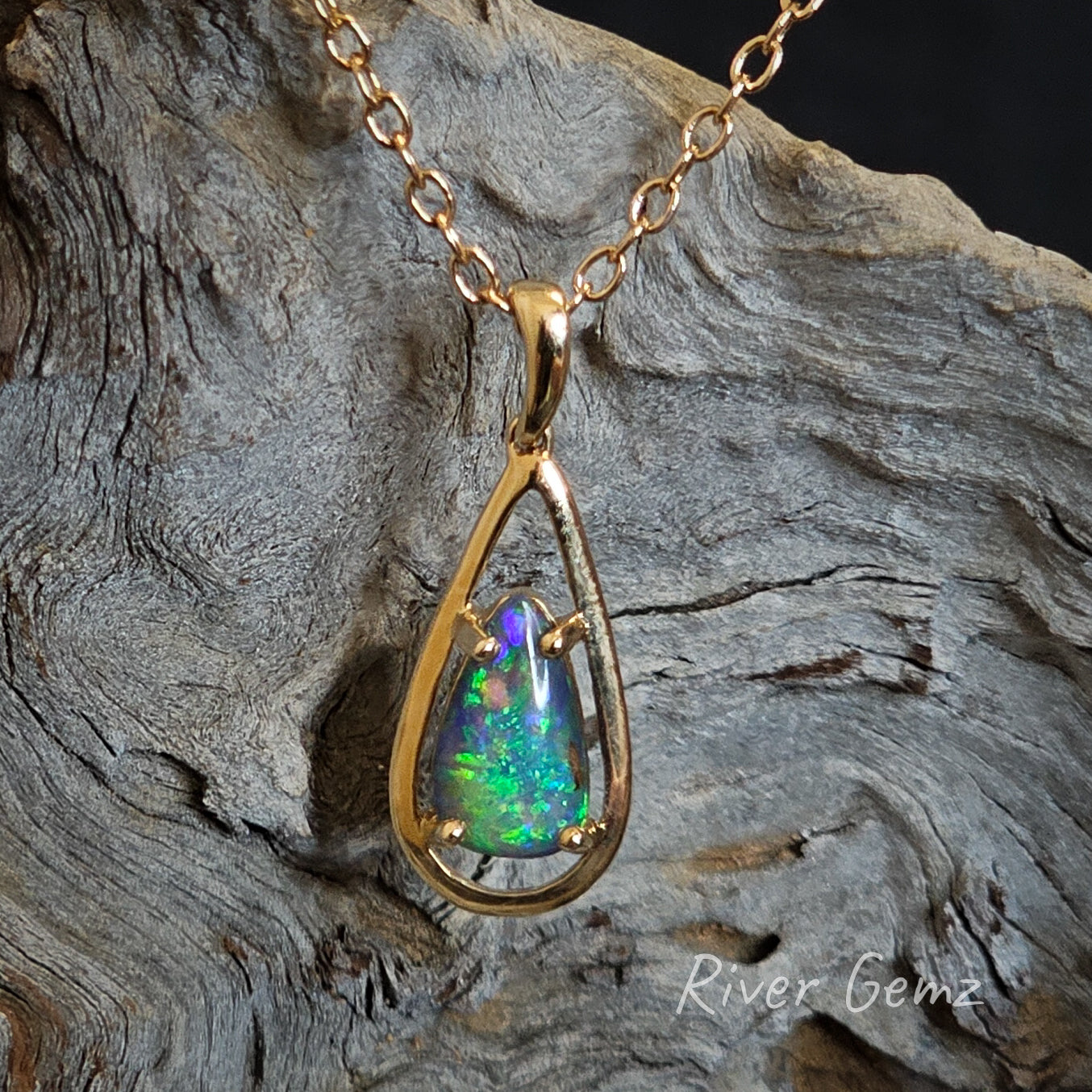 Tear drop shaped dark blue and green boulder opal claw set  in tear drop shaped gold necklace.