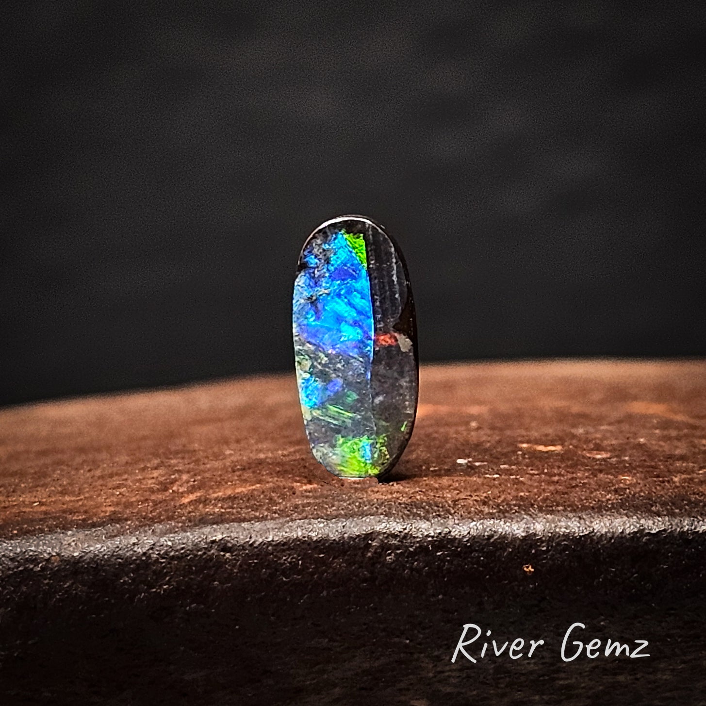 Multicolored opal stone on a dark background with 'River Gemz' branding.