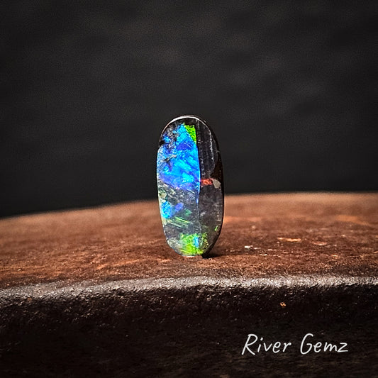 Multicolored opal stone on a dark background with 'River Gemz' branding.