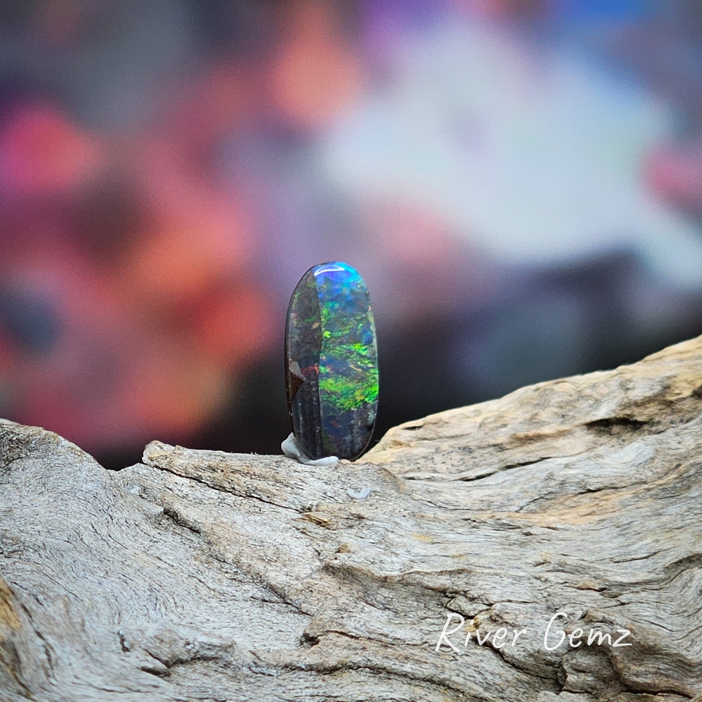 Oval shaped dark opal with swirls of blue and green and a dark patch on the left side from top to bottom.