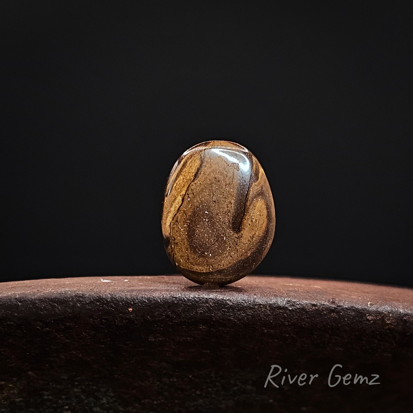 Rear view of stone showing the iron stone matrix of the boulder opal on a dark background with 'River Gemz' branding.