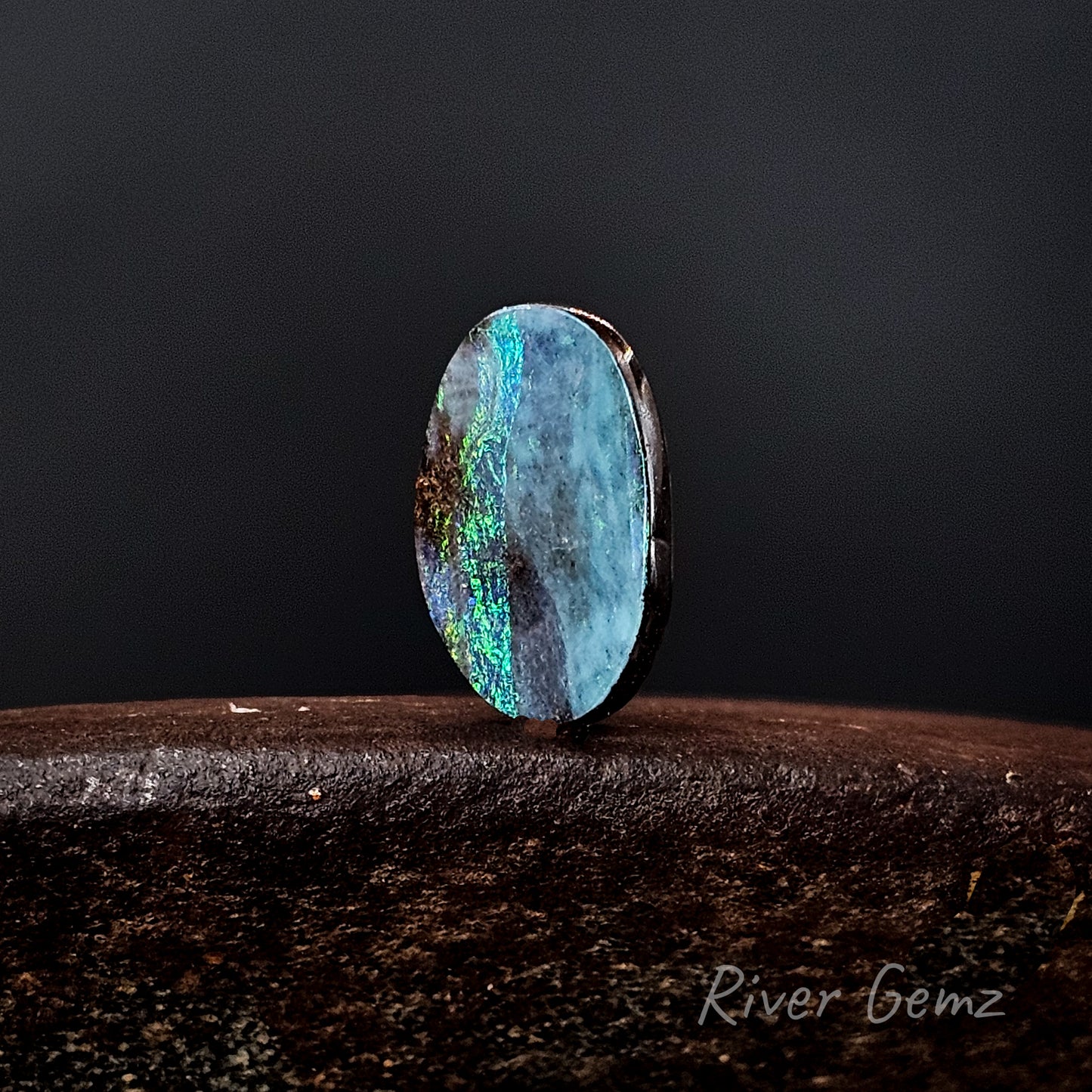 Blue and green unset boulder opal stone on a dark background with 'River Gemz' branding.