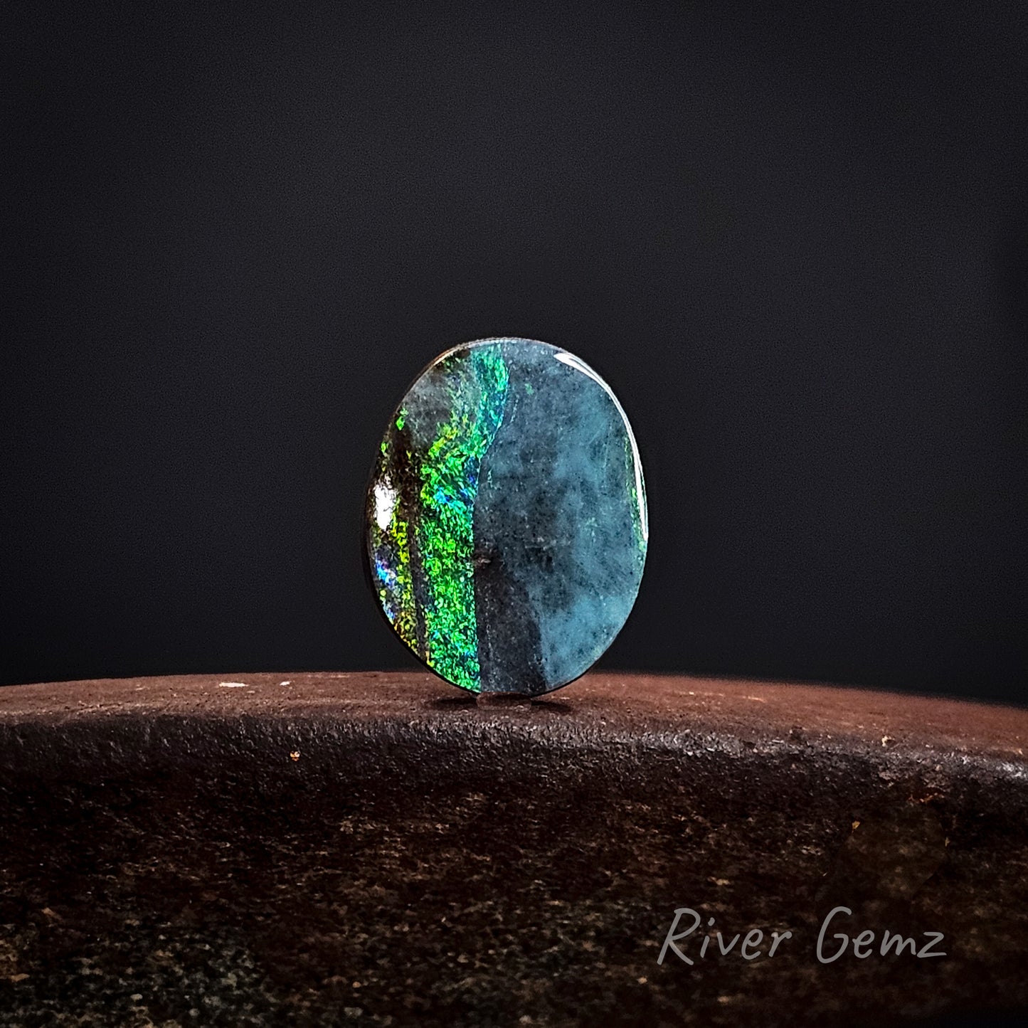 Opal stone with colorful patterns on a dark background, branded 'River Gemz'.