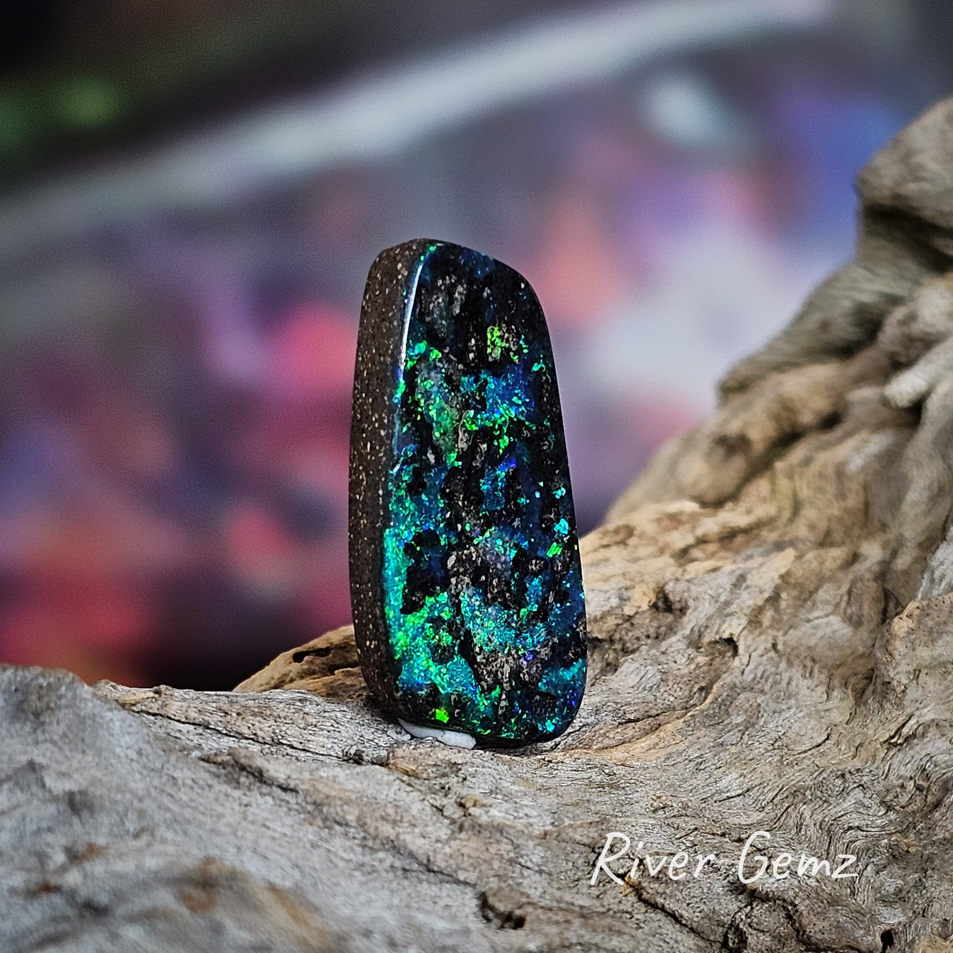 An rounded corner rectangular shaped dark opal with blues and greens throughout.