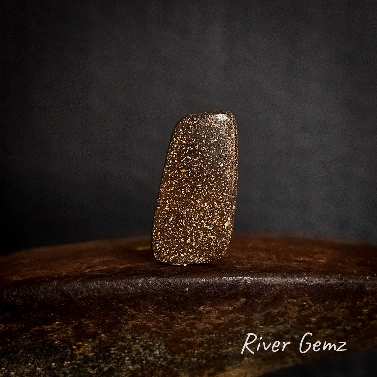 Back view of stone showing the speckled brown matrix of the boulder opal on a dark background with 'River Gemz' branding.