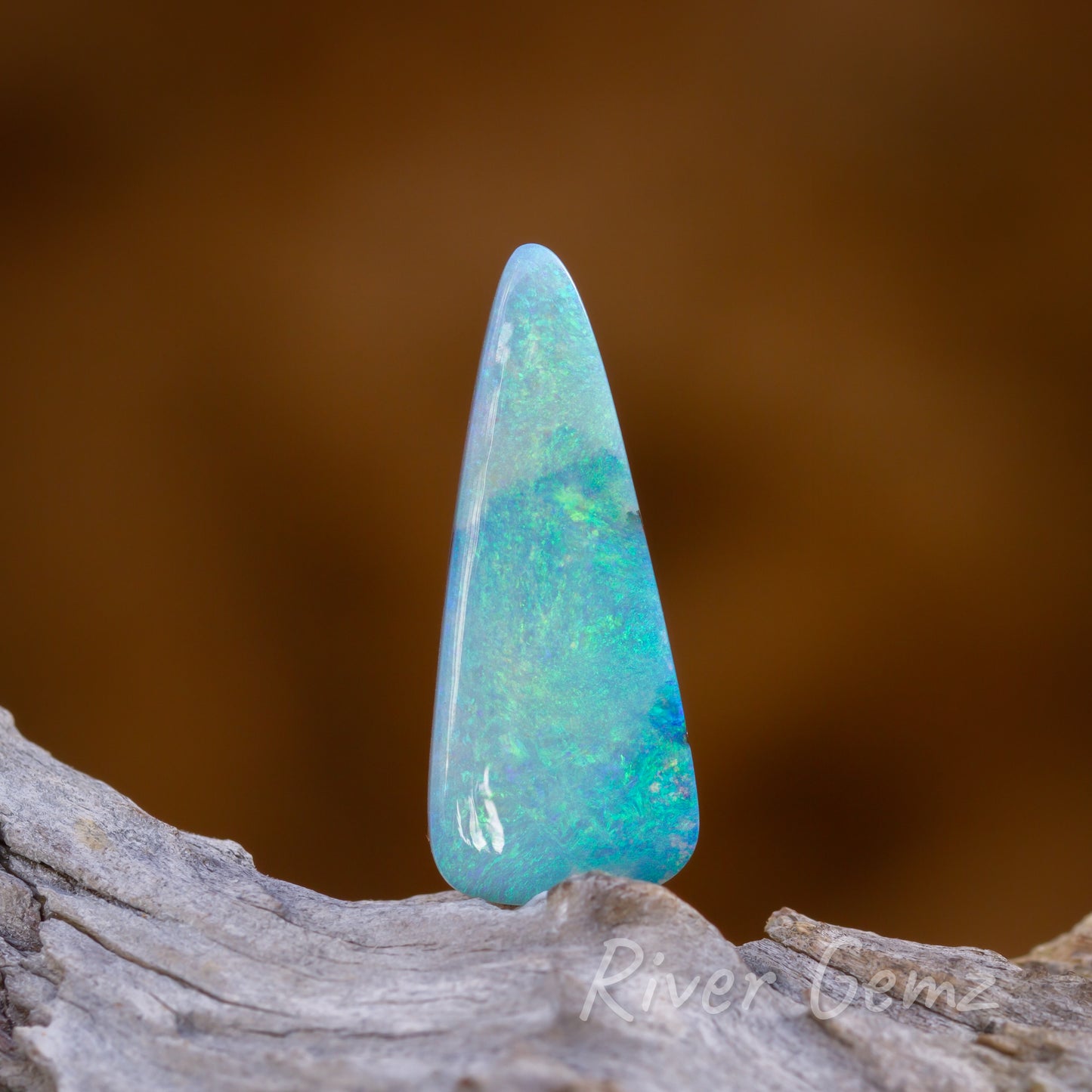 Tear drop shaped blue-green opal erect on light grey textured wood.