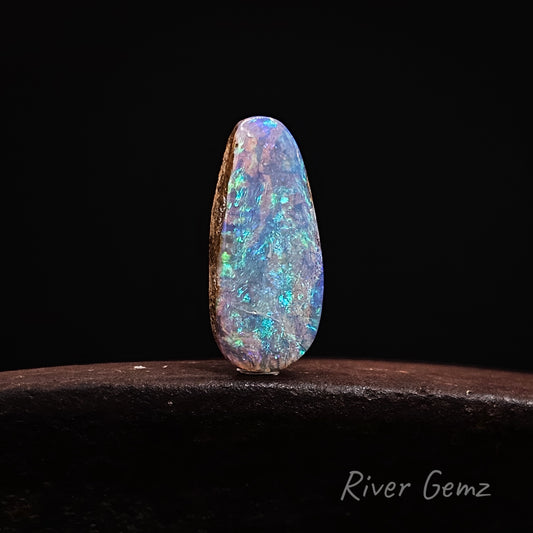 Multicolored opal stone on a dark background with 'River Gemz' branding.