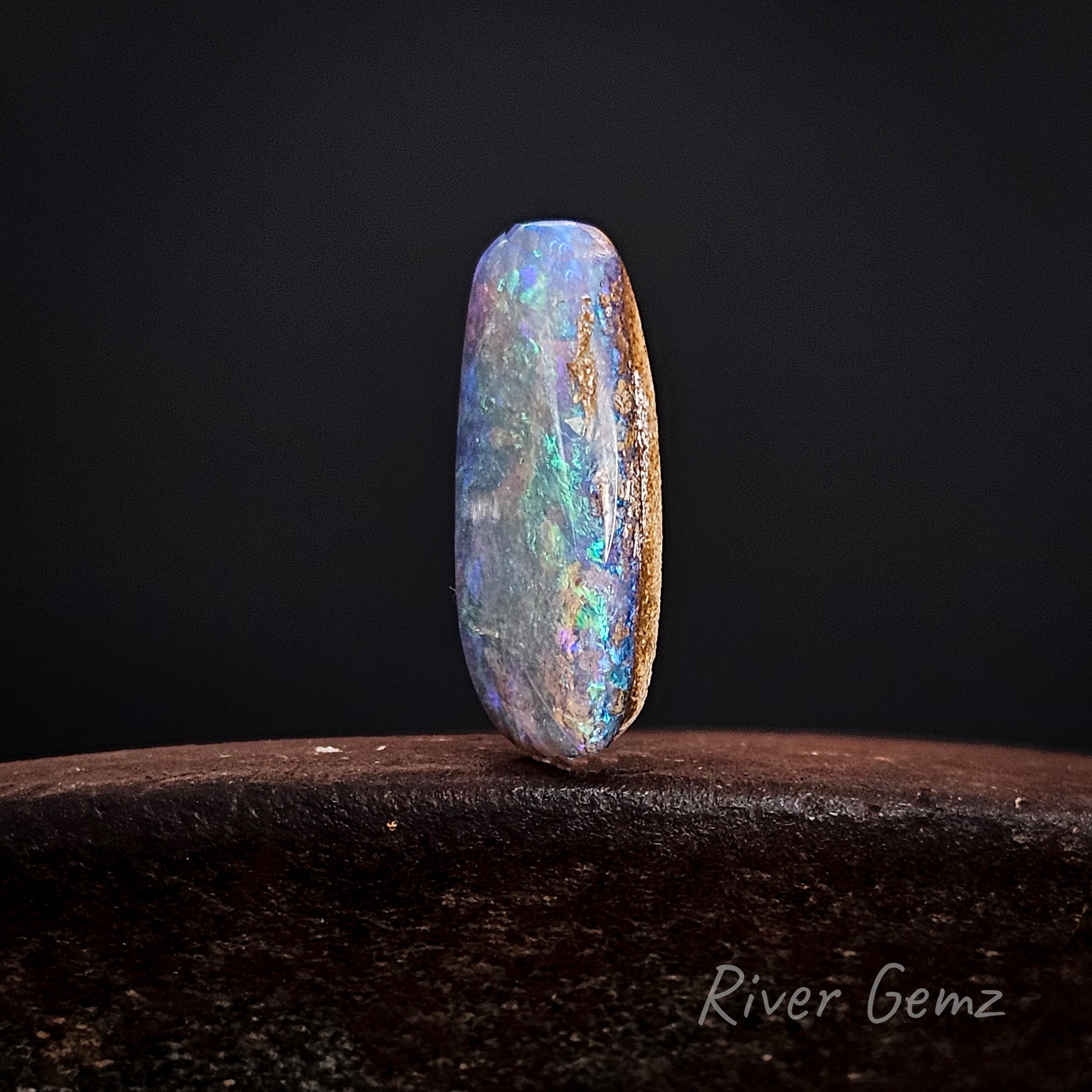 Multicolored opal stone on a dark background with 'River Gemz' branding.