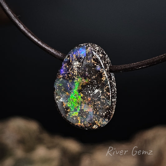 Opal pendant on a brown cord with a blurred natural rock background, featuring the brand 'River Gemz'.