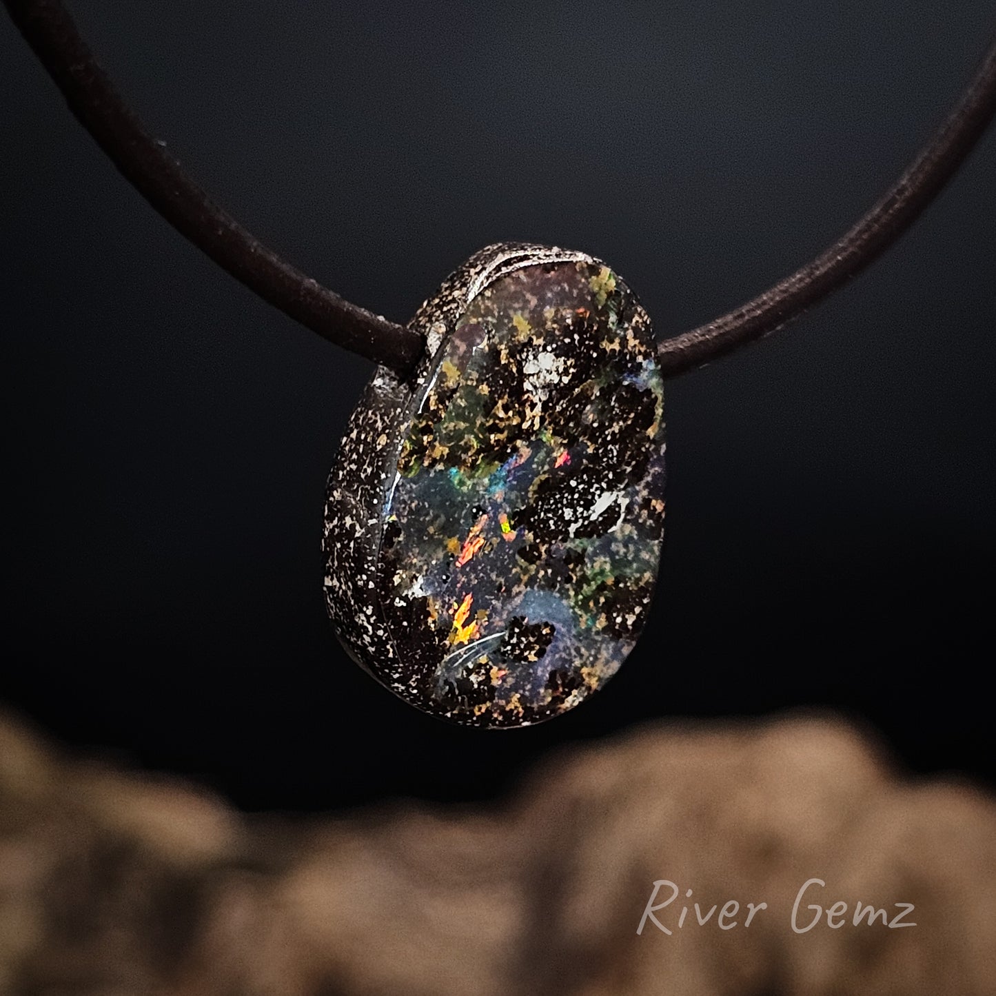 Multicolored stone pendant on a dark background with 'River Gemz' branding.