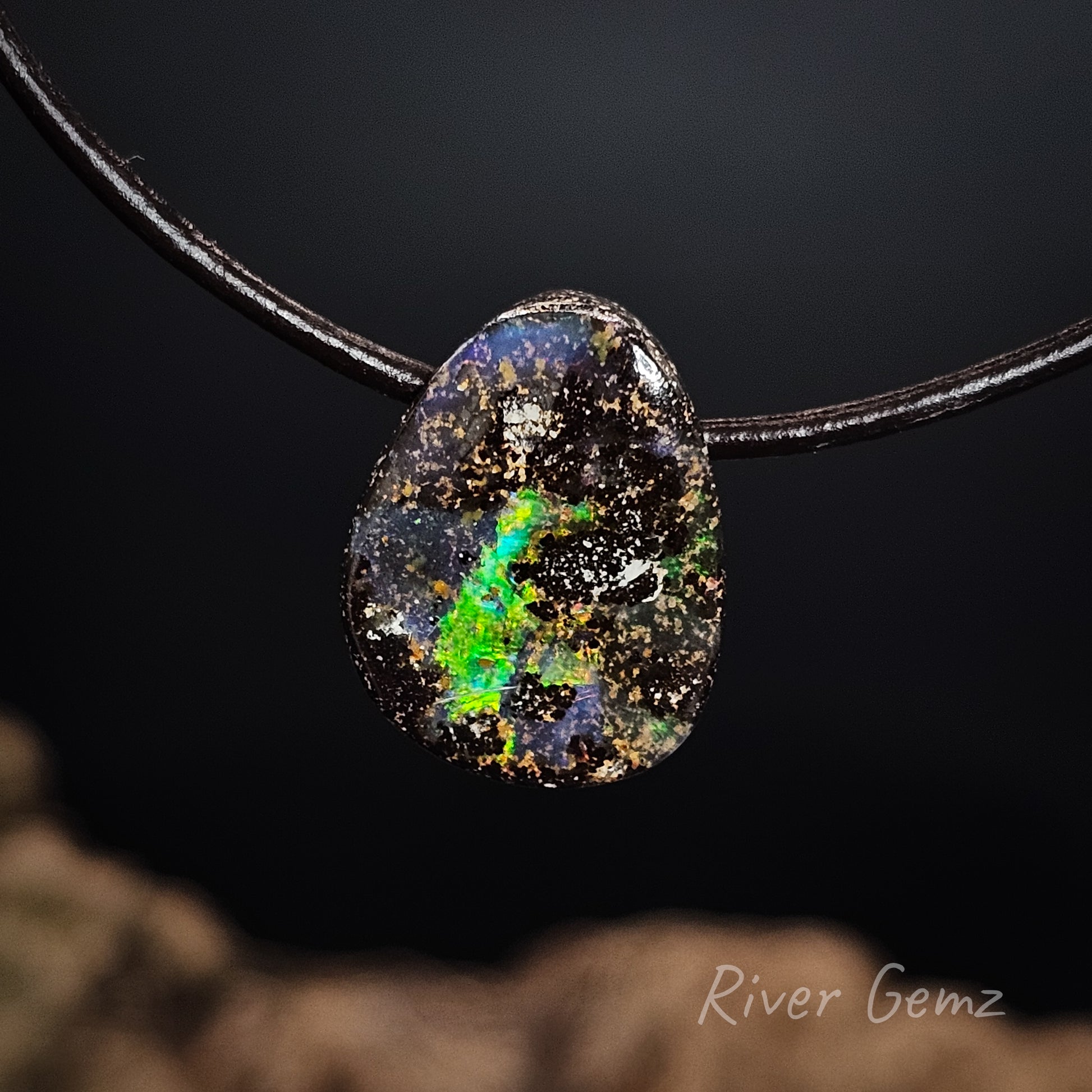Opal pendant on a black cord with a blurred natural background