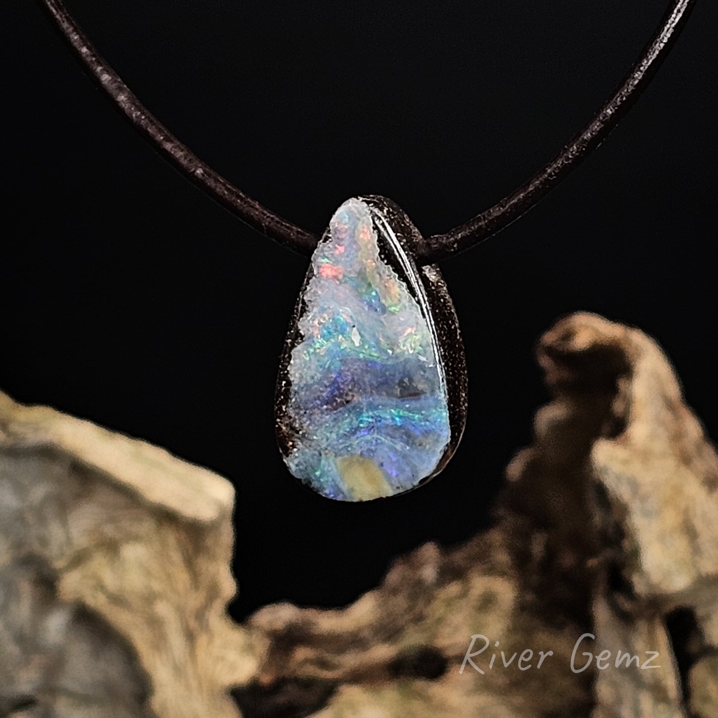 Opal pendant on a dark cord with a natural rock background, featuring 'River Gemz' branding.
