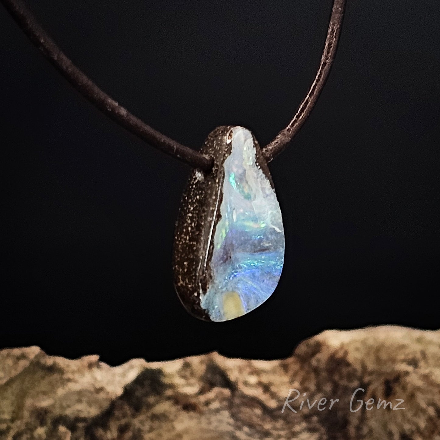 Opal pendant on a dark cord against a dark background with 'River Gemz' branding.