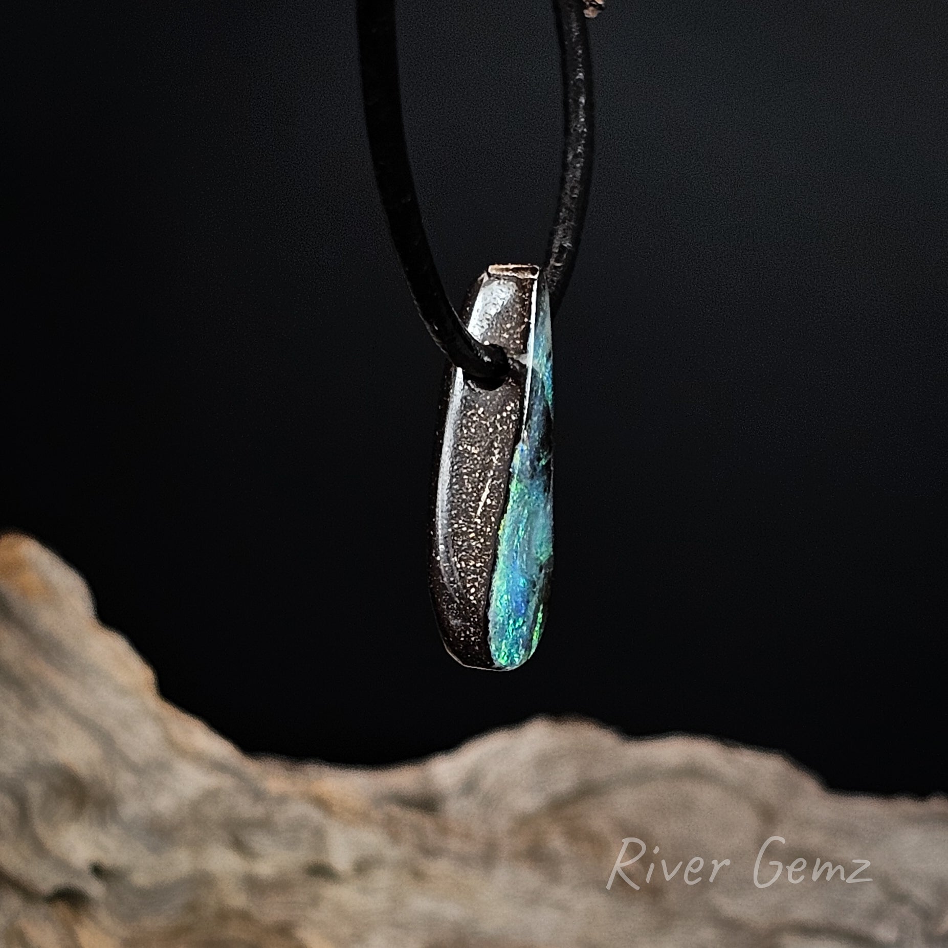 Opal pendant on a black cord with a dark background and 'River Gemz' branding.