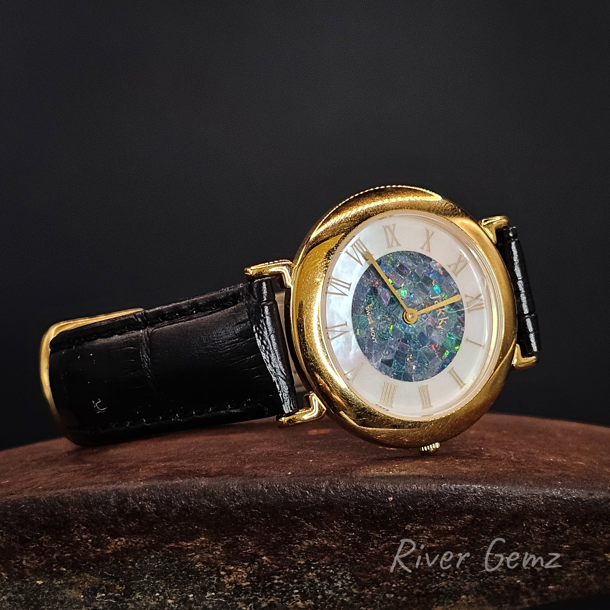 Vintage watch with opal dial and black leather strap and gold case on a dark background.