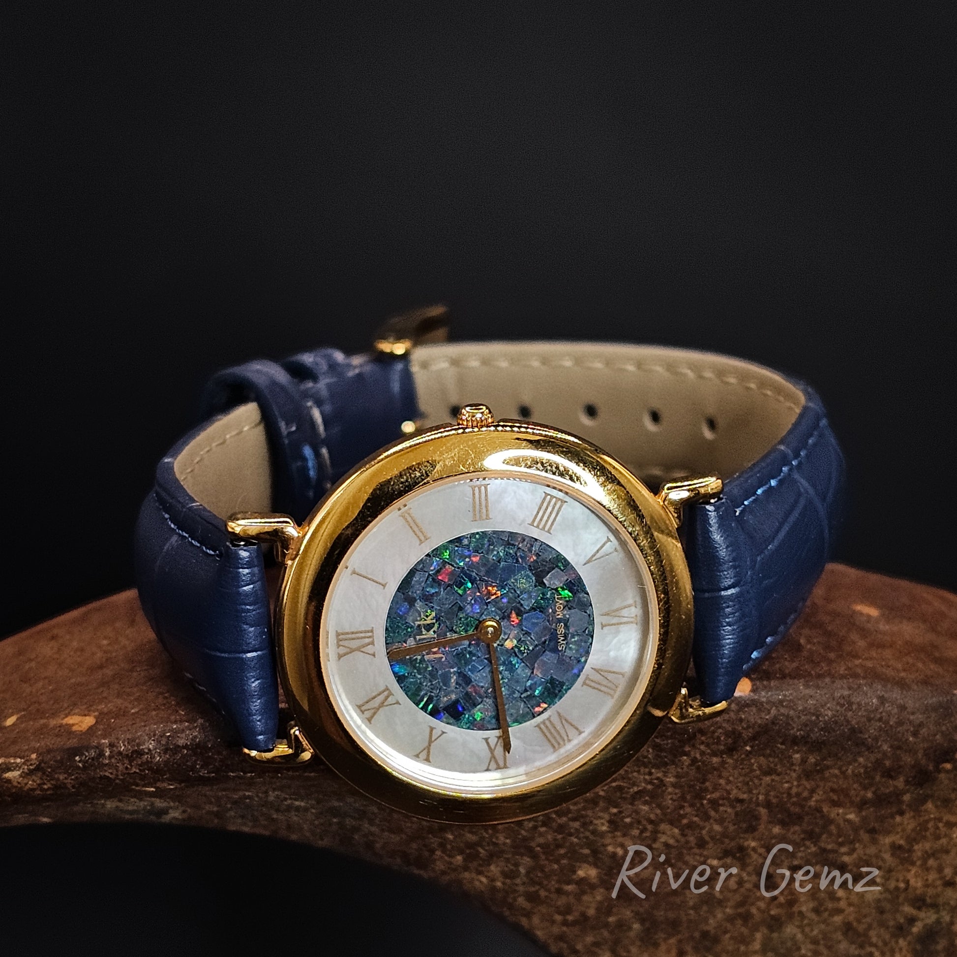 Watch with blue strap and gold case on a dark background, featuring 'River Gemz' branding.