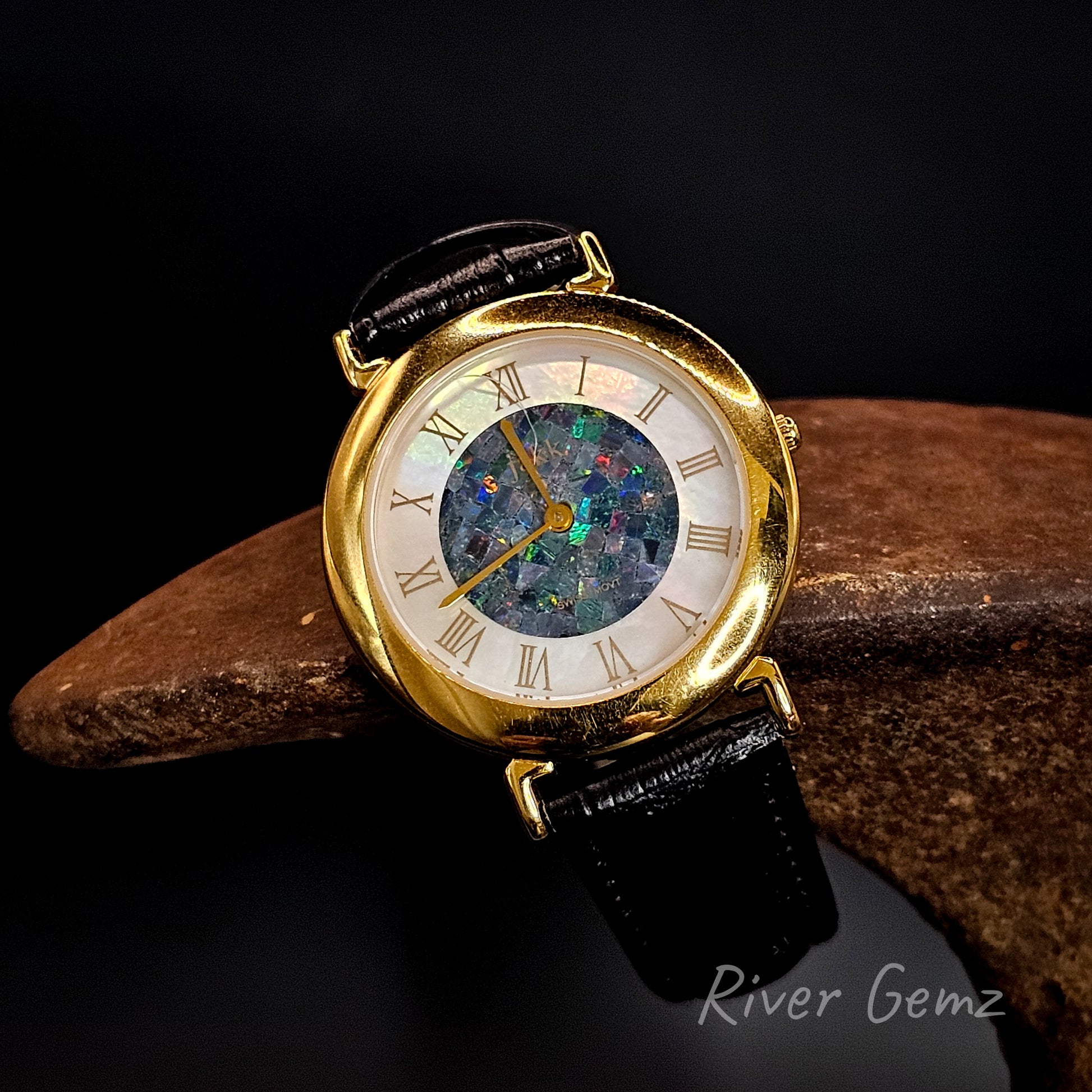 Gold watch with a unique face on a dark background, featuring the brand 'River Gemz'.