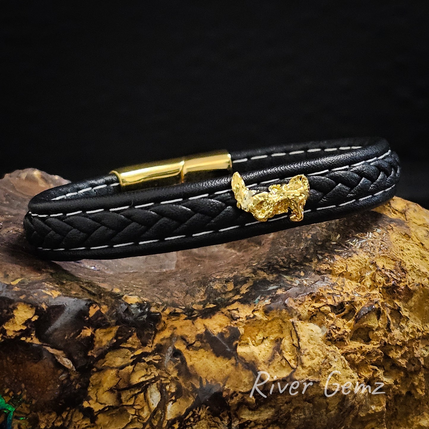 Vibrant yellow gold natural nugget contrasts against the black leather bracelet. Directly opposite the nugget is the gold coloured slide-type locking mechanism.