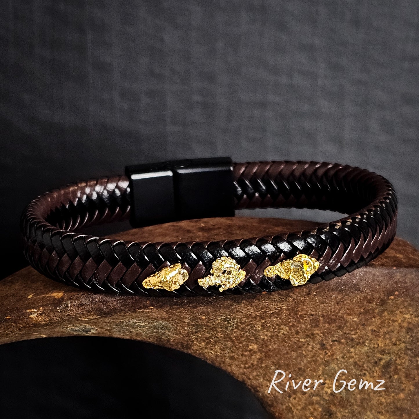 Brown and black braided leather bracelet with gold nuggets on a dark background, featuring the brand 'River Gemz'.