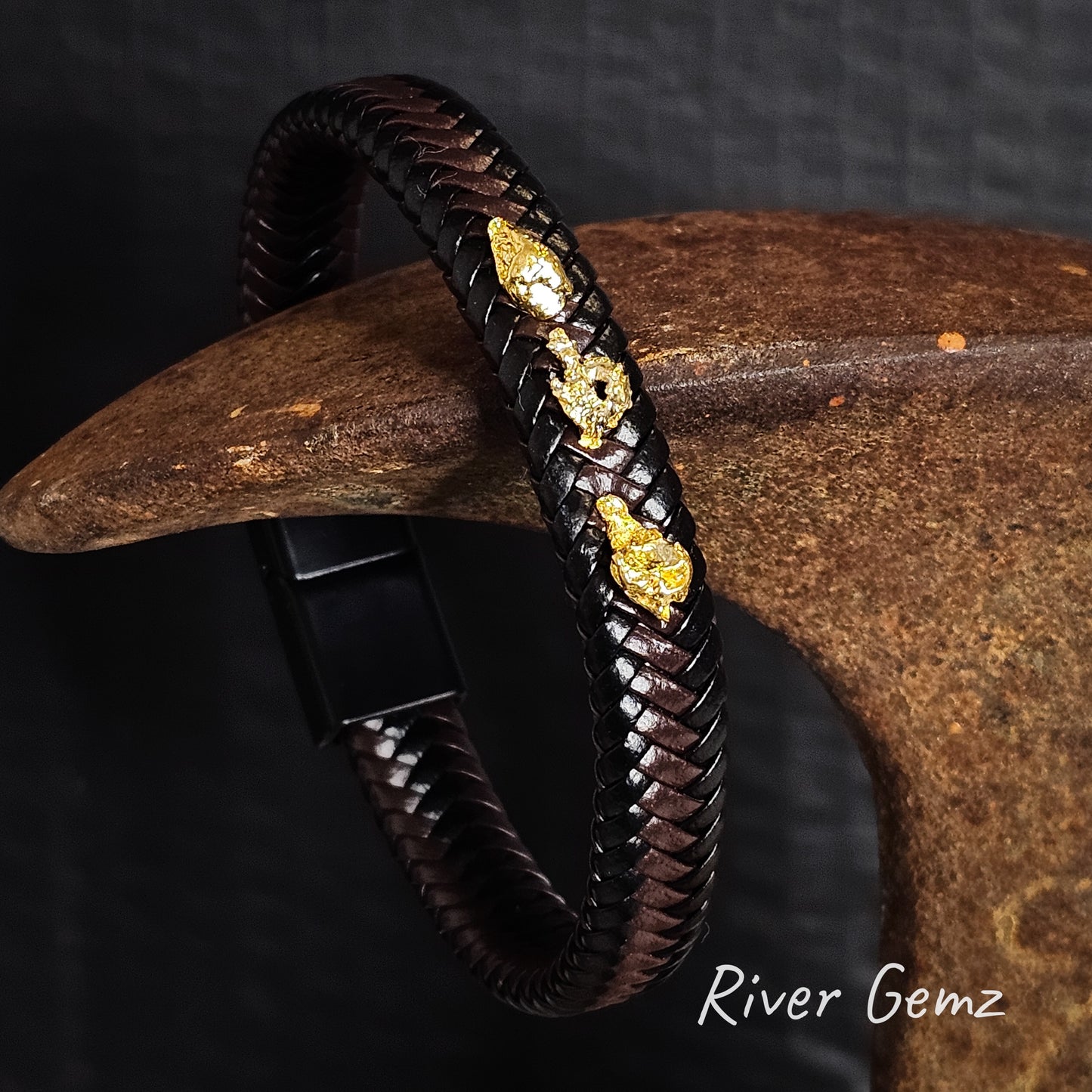 Brown and black braided leather bracelet with three gold nuggets on a dark background, branded 'River Gemz'.
