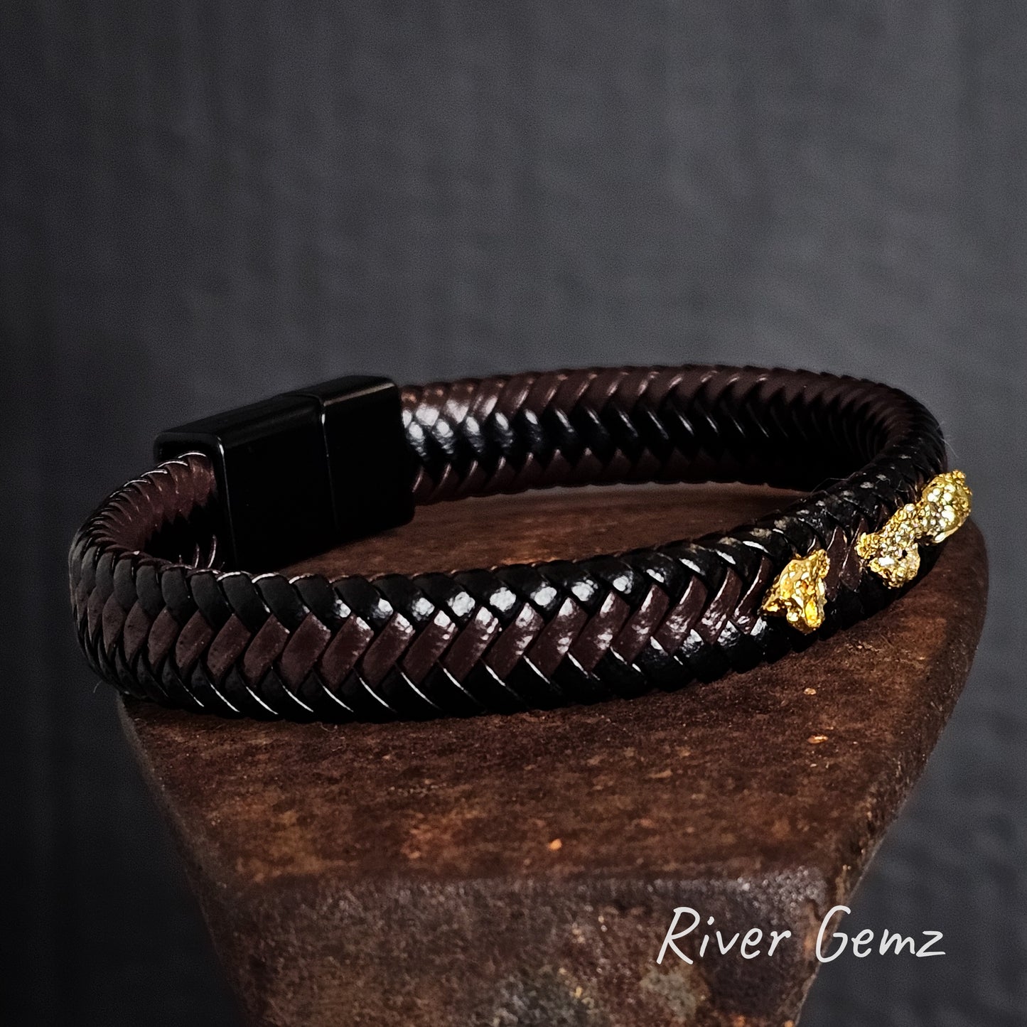 Brown braided leather bracelet with gold nuggets on a dark background, featuring the brand 'River Gemz'.