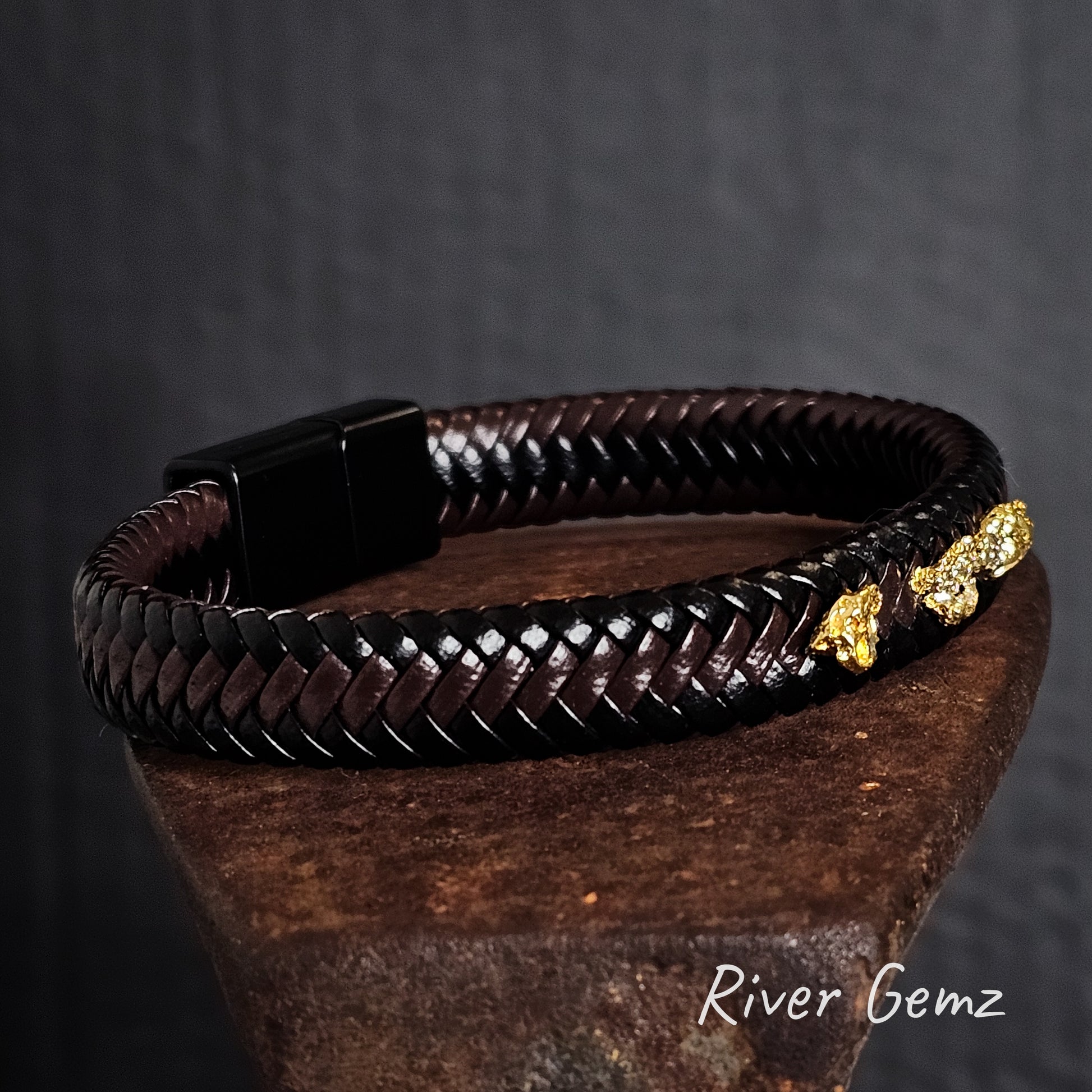 Brown braided leather bracelet with gold nuggets on a dark background, featuring the brand 'River Gemz'.