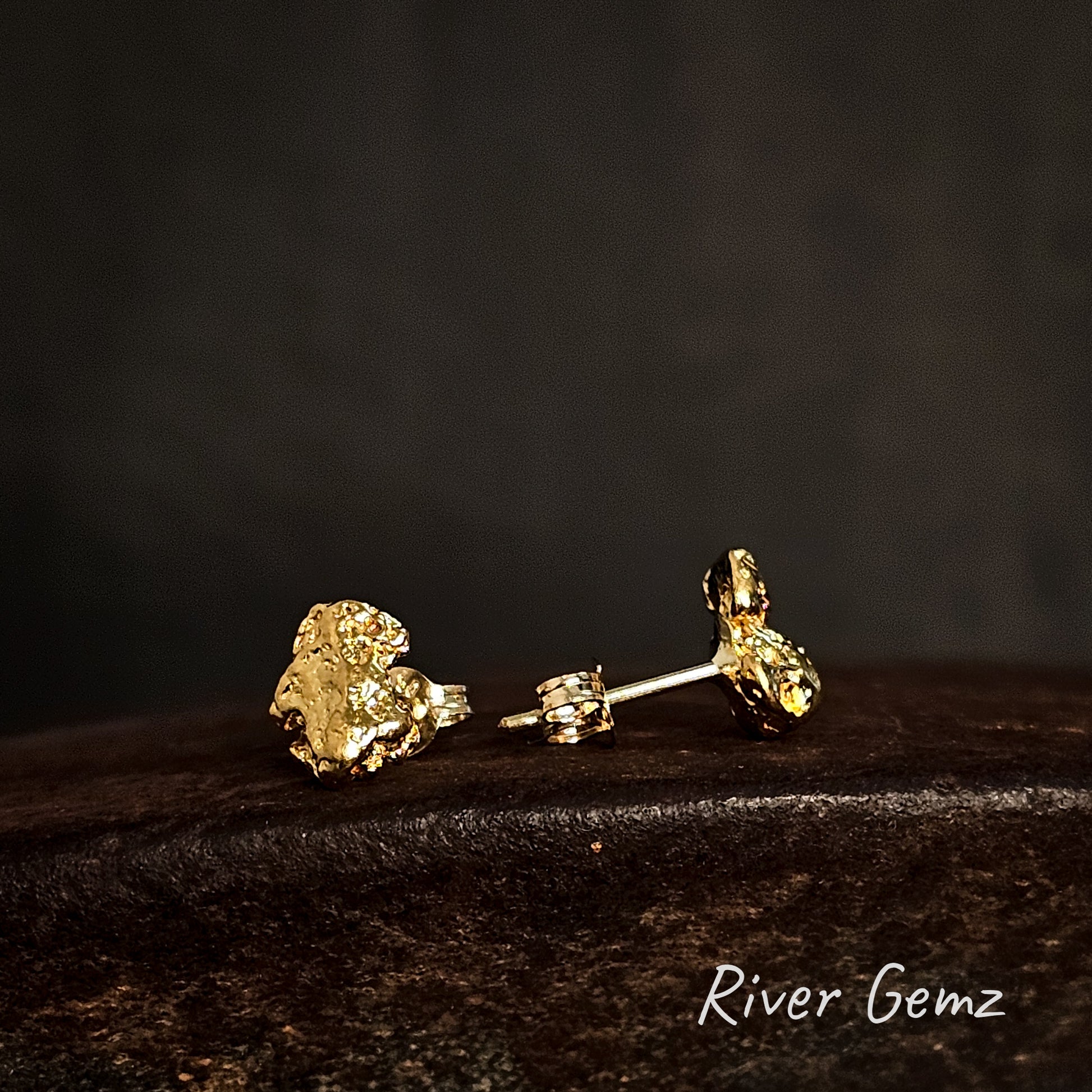 Gold earrings on a dark surface with 'River Gemz' branding.