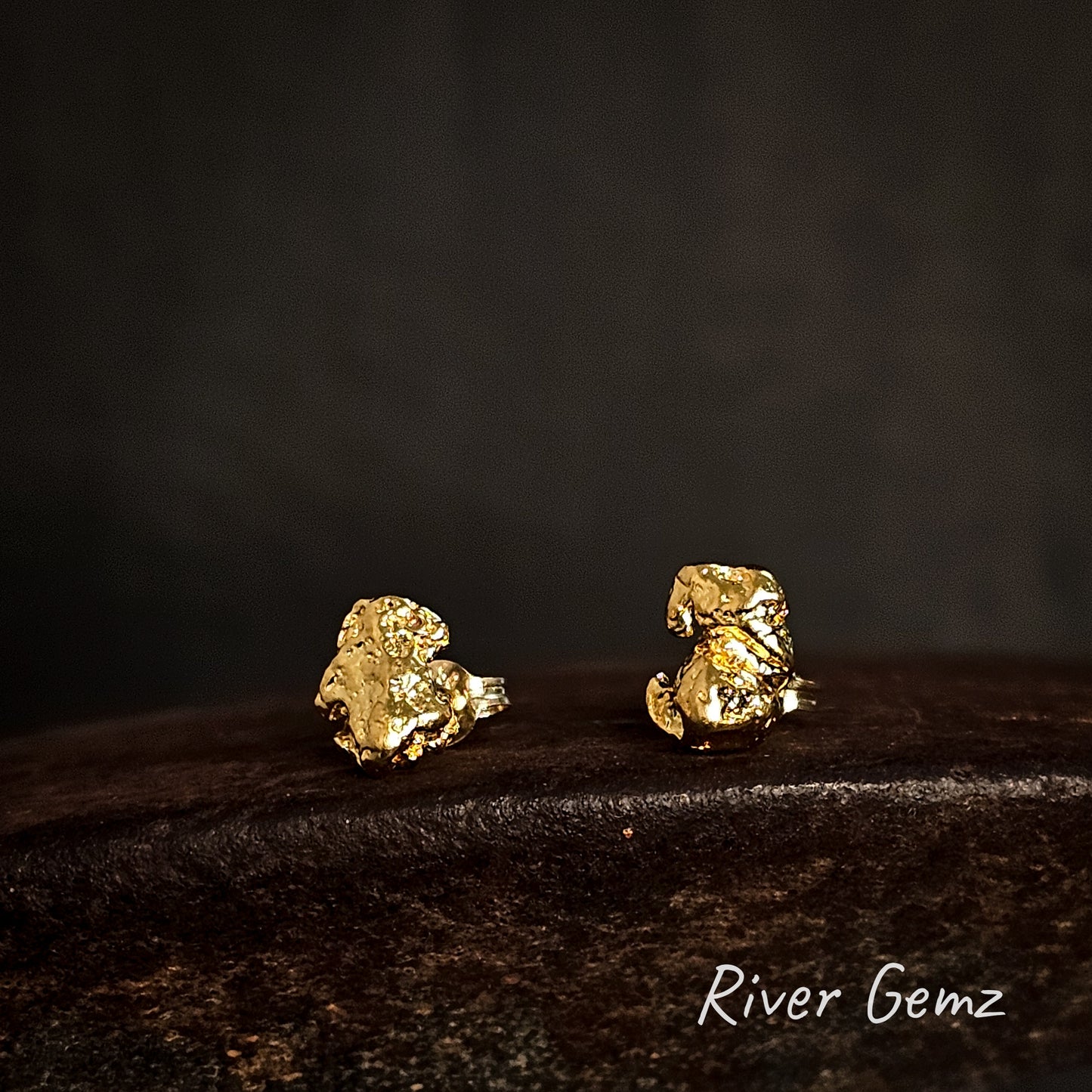 Gold nugget earrings on a dark surface with 'River Gemz' branding.