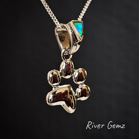 Triangle-shaped dark green and blue crystal opal besel set in the bail of a paw print silver pendant.