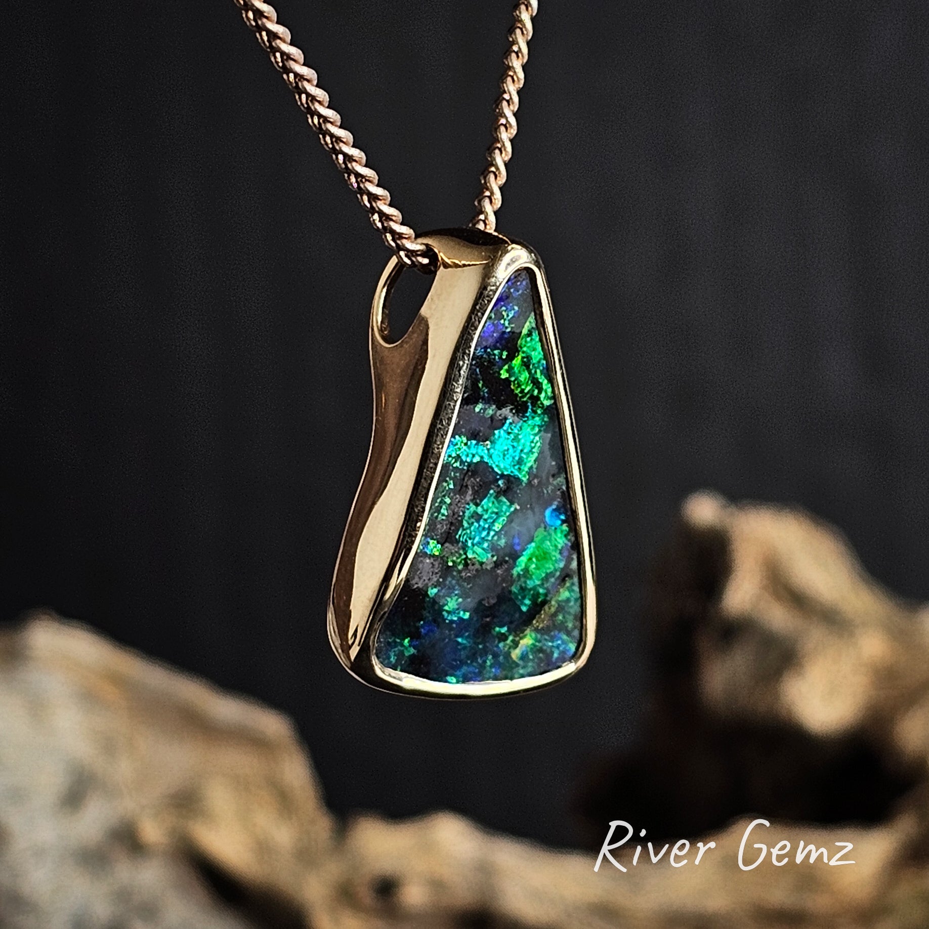 Gold pendant with a blue and green boulder opal on a dark background, featuring 'River Gemz' branding.