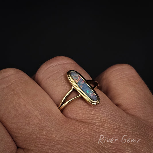 Oval shaped multi-coloured opal worn on ring finger of right hand against a black back ground.