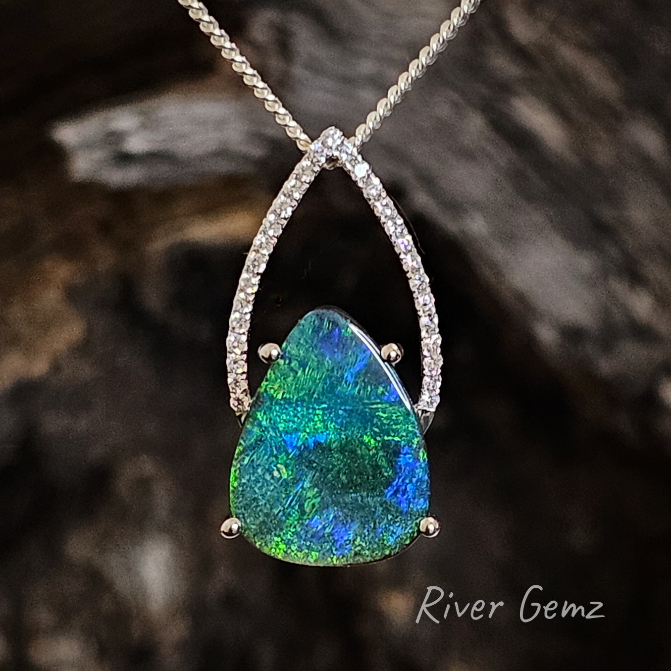 Blue and green tear drop shaped boulder opal claw set in white gold and a "bishops mitre" of diamonds above the opal.